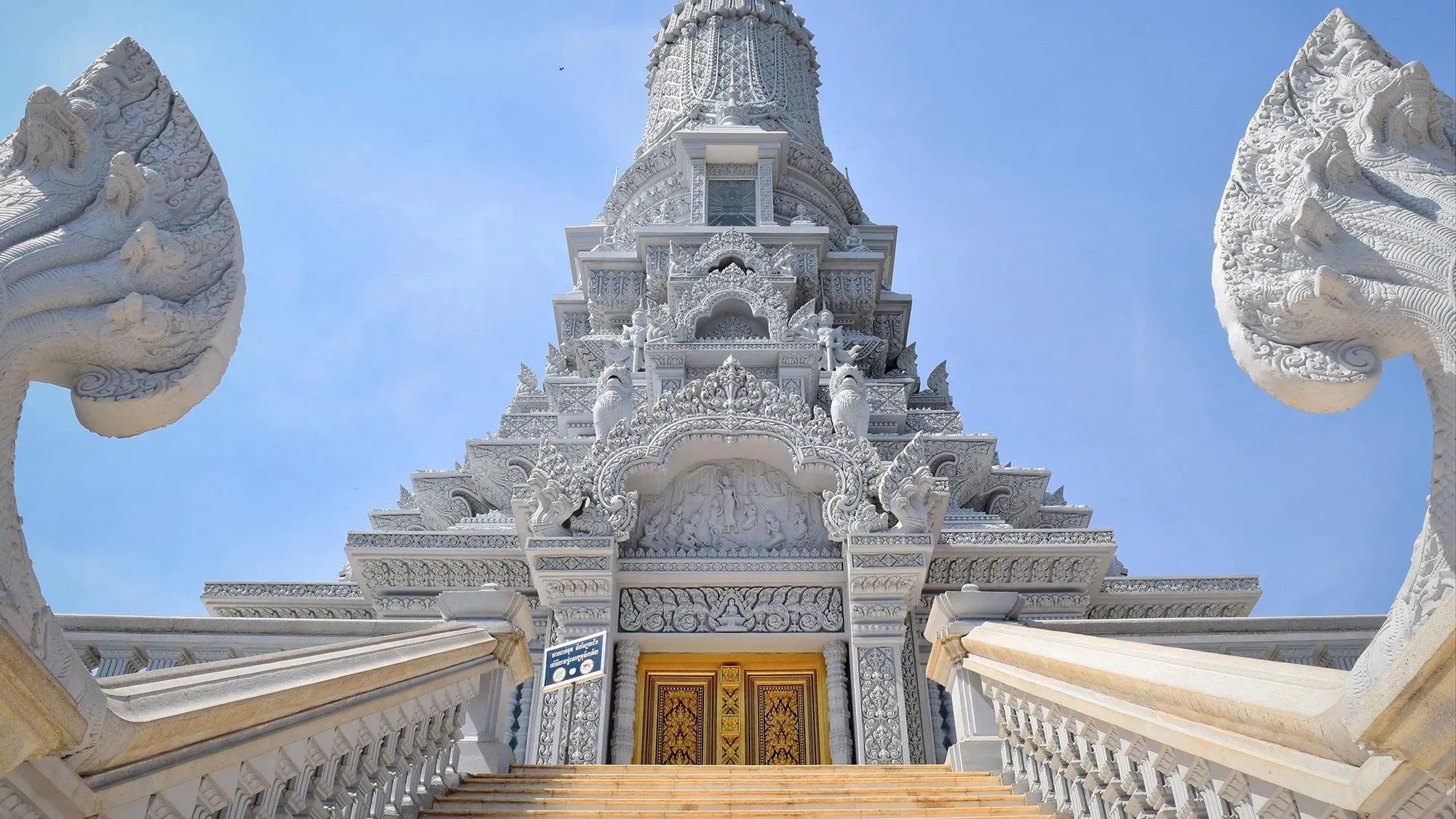 معبد مزخرف في أودونغ، كمبوديا، يظهر تفاصيله المعمارية الرائعة وألوانه الزاهية، محاطاً بأعلام بوذية ودرجات تؤدي إلى القمة.