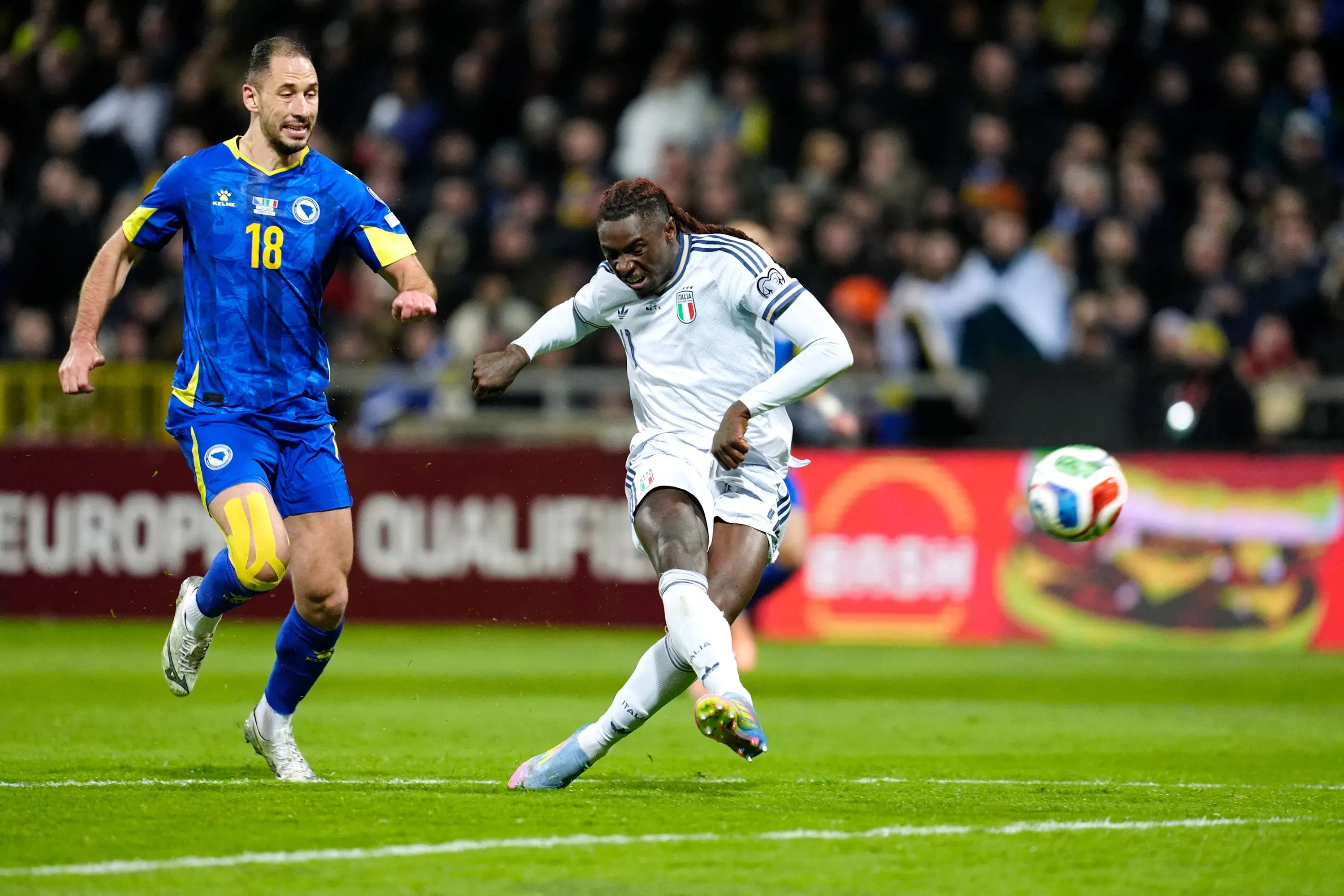 لاعب إيطالي يسدد الكرة أثناء مباراة فاصلة ضد البوسنة والهرسك، مع وجود مدافع بوسني يلاحقه، في لحظة حاسمة من التصفيات.