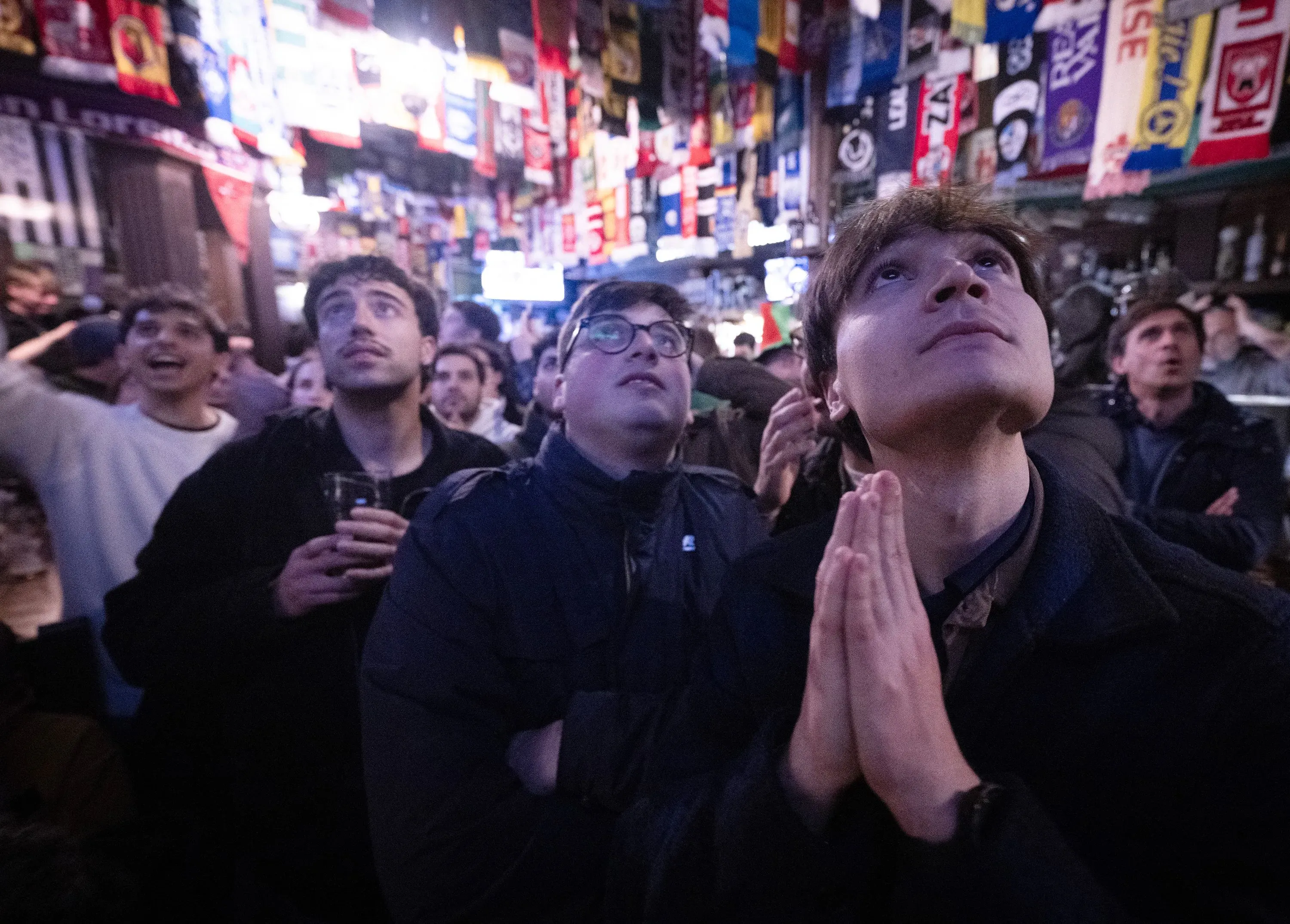 مشجعون إيطاليون في حانة يتابعون مباراة منتخبهم بقلق، مع تواجد الأعلام الرياضية في الخلفية، معبرين عن مشاعر التوتر والأمل.