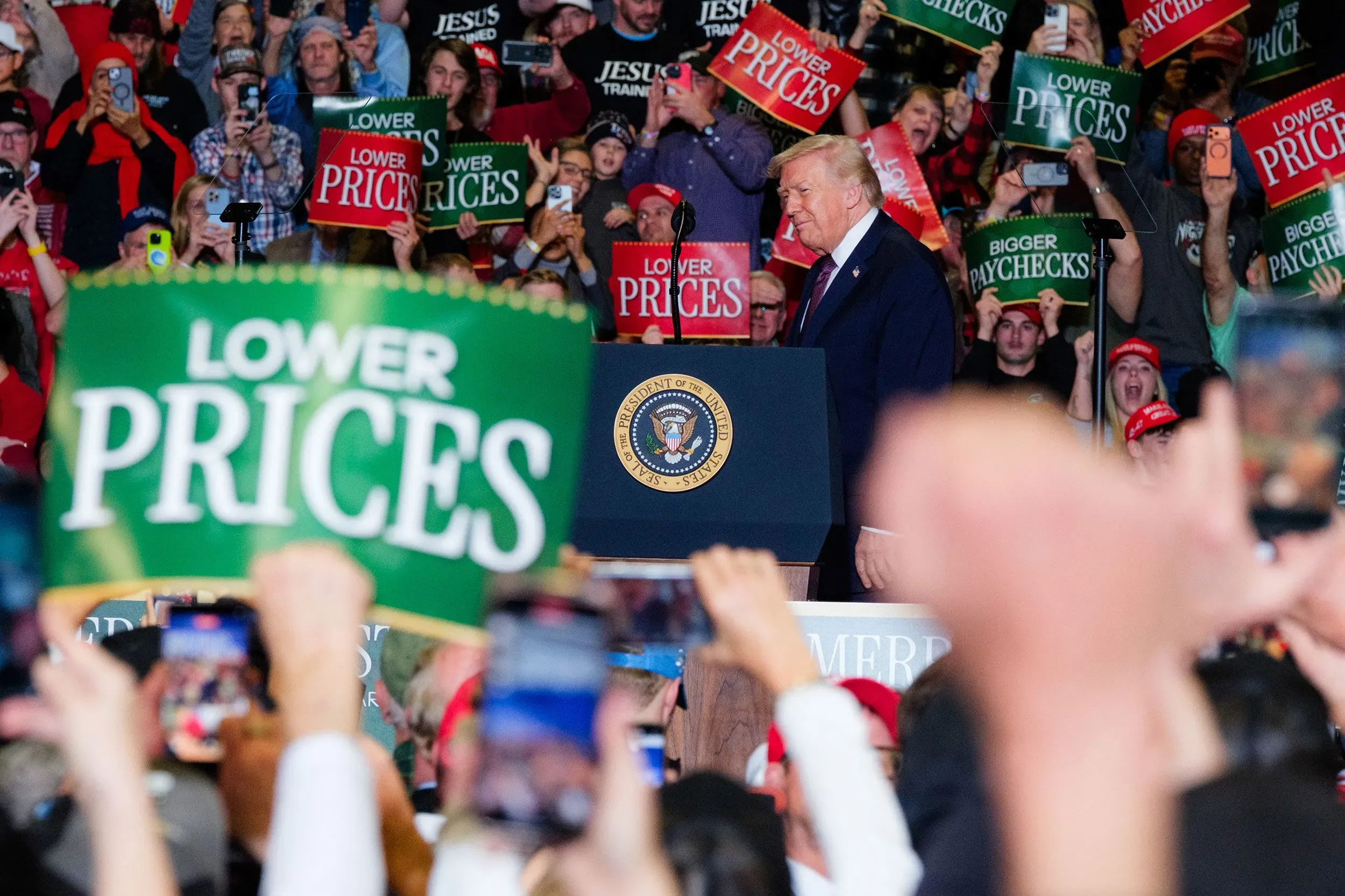 ترامب يتحدث في تجمع حاشد، حيث يحمل الحضور لافتات تطالب بخفض الأسعار وزيادة الرواتب، مما يعكس القلق بشأن الوضع الاقتصادي.
