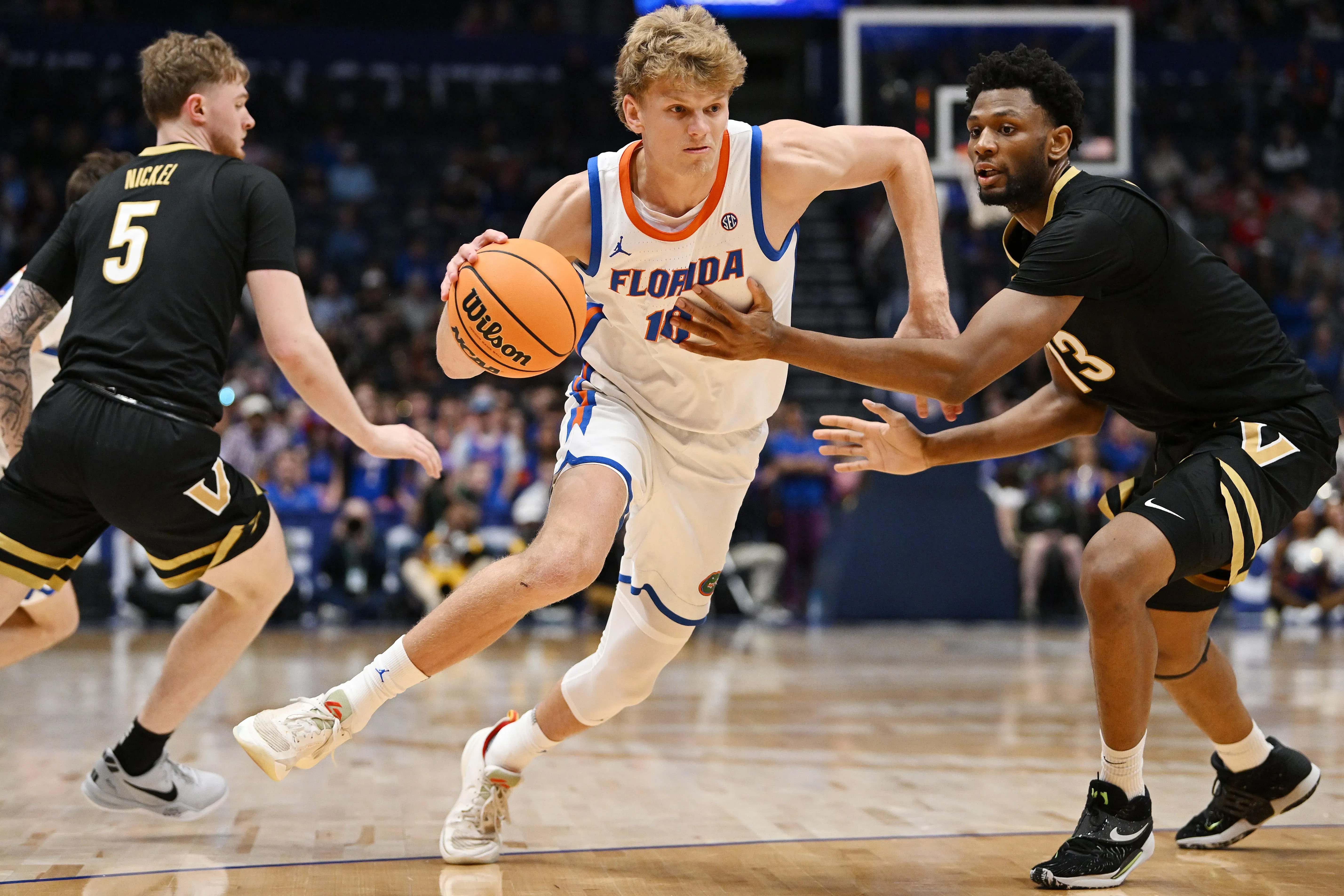 لاعب كرة سلة من فريق فلوريدا يتجاوز مدافعين أثناء مباراة NCAA، مع كرة سلة في يده، في أجواء تنافسية حماسية.