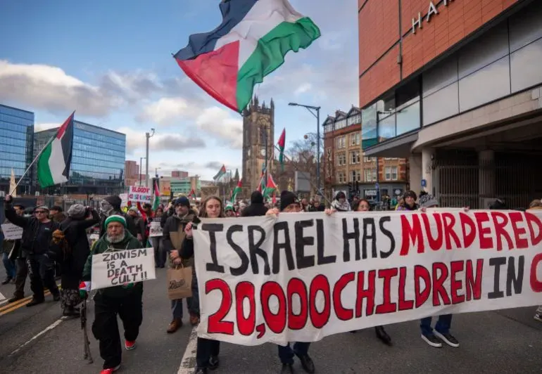 محتجون يحملون لافتات في مظاهرة ضد الاحتلال الإسرائيلي، مع أعلام فلسطينية، في مشهد يعكس مطالبهم بالحرية والعدالة.