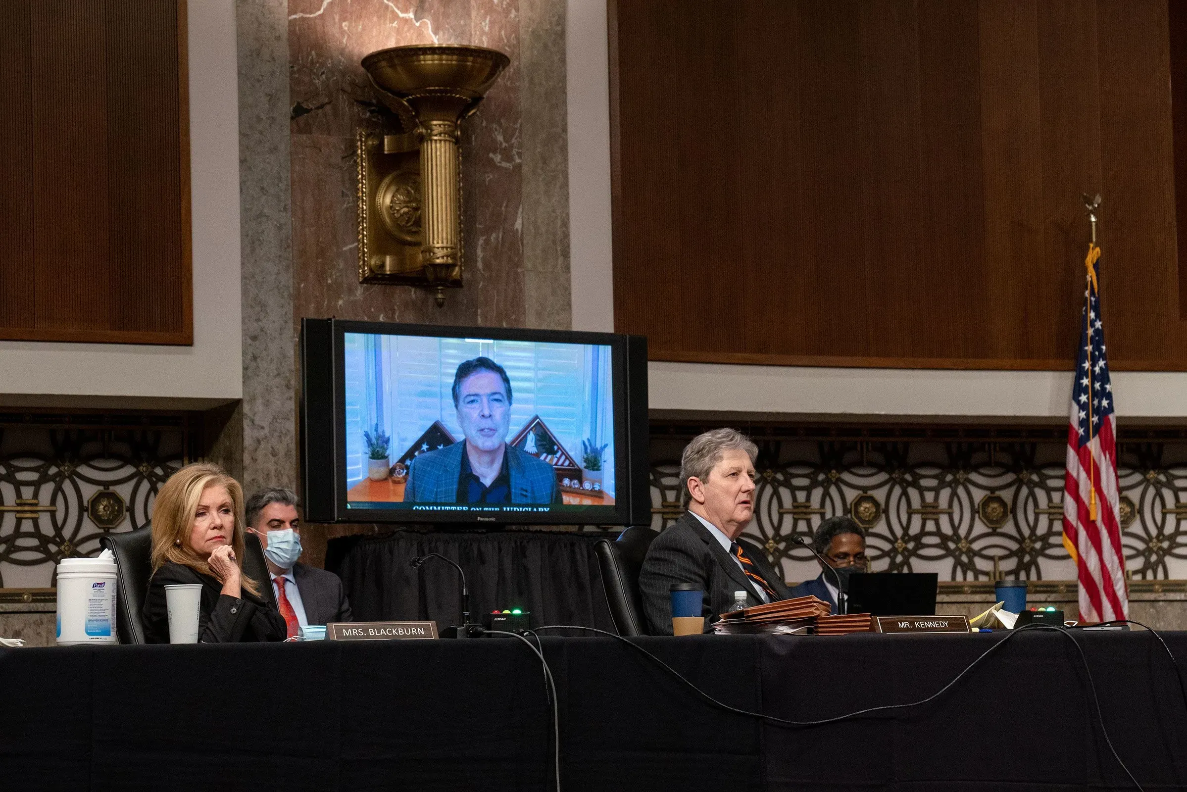 مدير مكتب التحقيقات الفيدرالي جيمس كومي خلال جلسة استماع برفقة مسؤولين آخرين، مع شاشة تظهر حديثه عبر الفيديو، في قاعة مجلس الشيوخ.