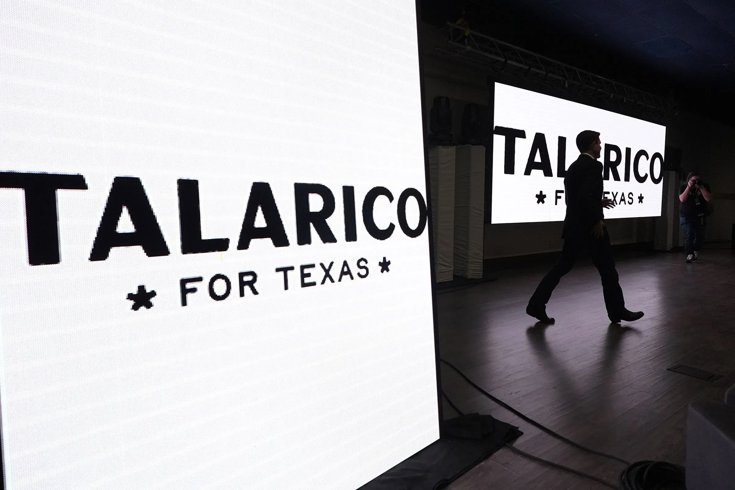 جيمس تالاريكو يسير نحو المنصة خلال حملته الانتخابية في تكساس، مع شعار "تالاريكو لتكساس" خلفه، في أجواء حماسية.