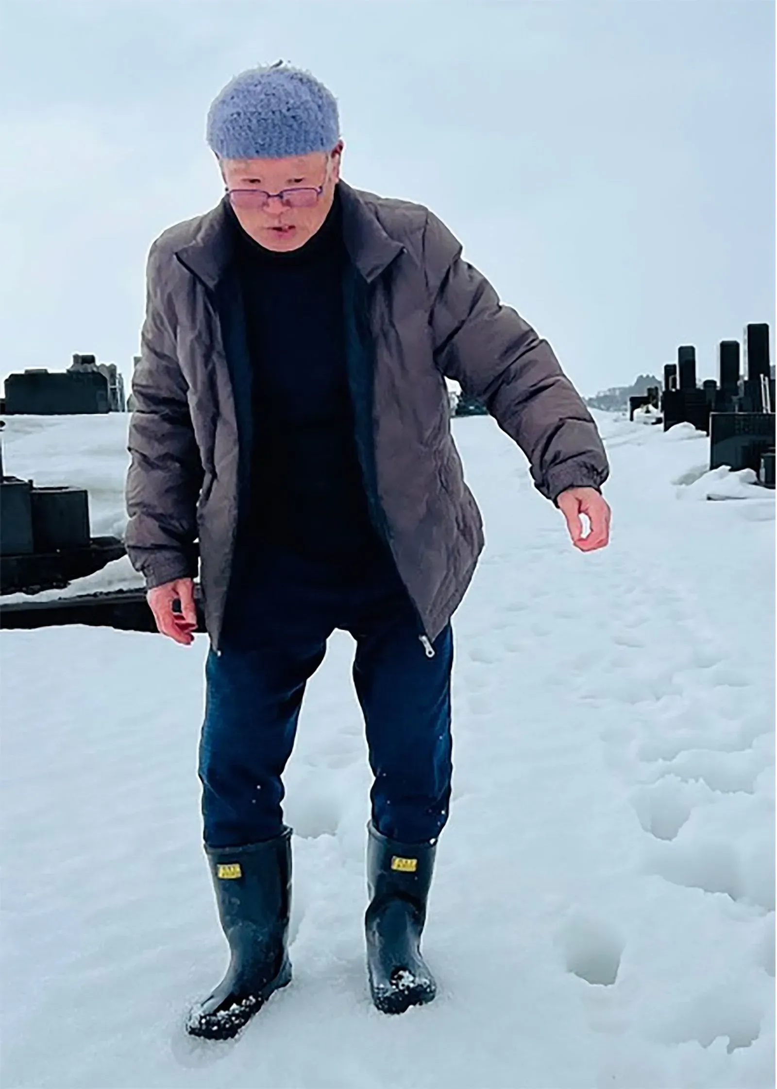 امرأة مسنّة ترتدي ملابس دافئة، تتنقل بصعوبة في الثلوج الكثيفة في شمال اليابان، تعكس تحديات الشتاء القاسي.