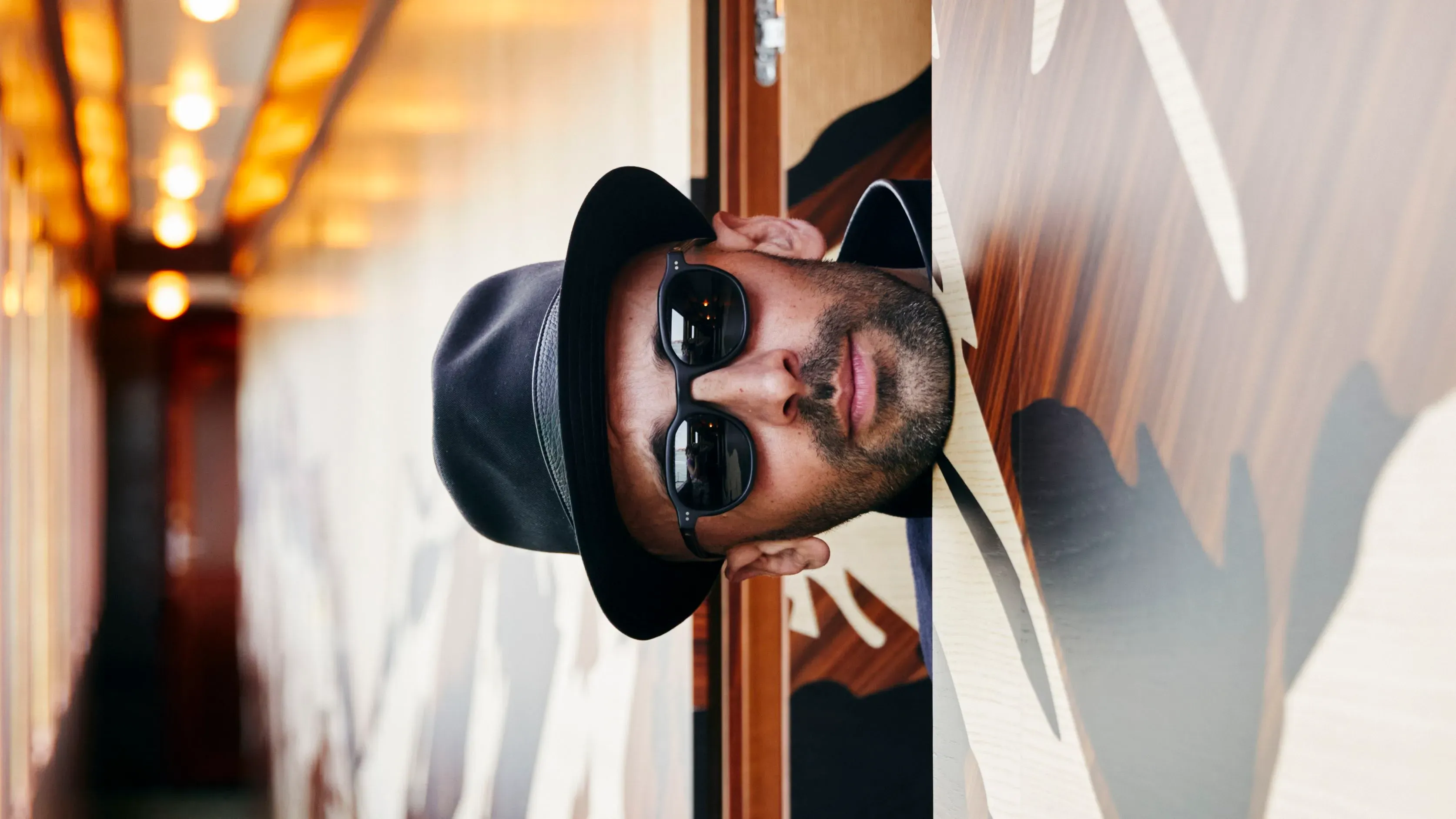 صورة لفنان الشارع والمصور JR داخل عربة قطار فاخرة، مع تفاصيل فنية معمارية مميزة، تعكس مشروعه "L'Observatoire" في بينالي البندقية.