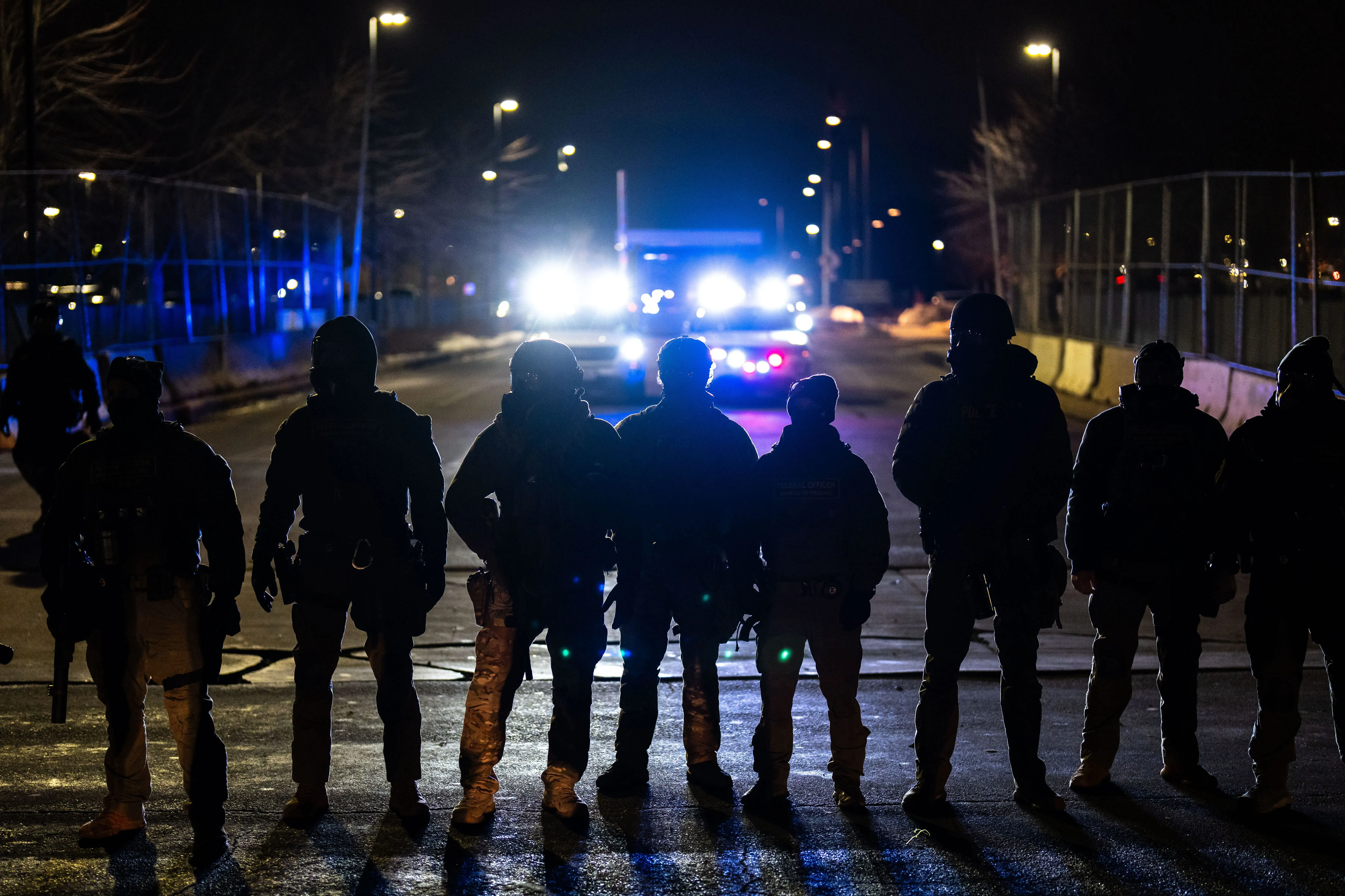 مجموعة من العملاء الفيدراليين في ملابس عسكرية، يقفون في صف واحد تحت الأضواء الساطعة، في سياق الاحتجاجات في مينيسوتا.