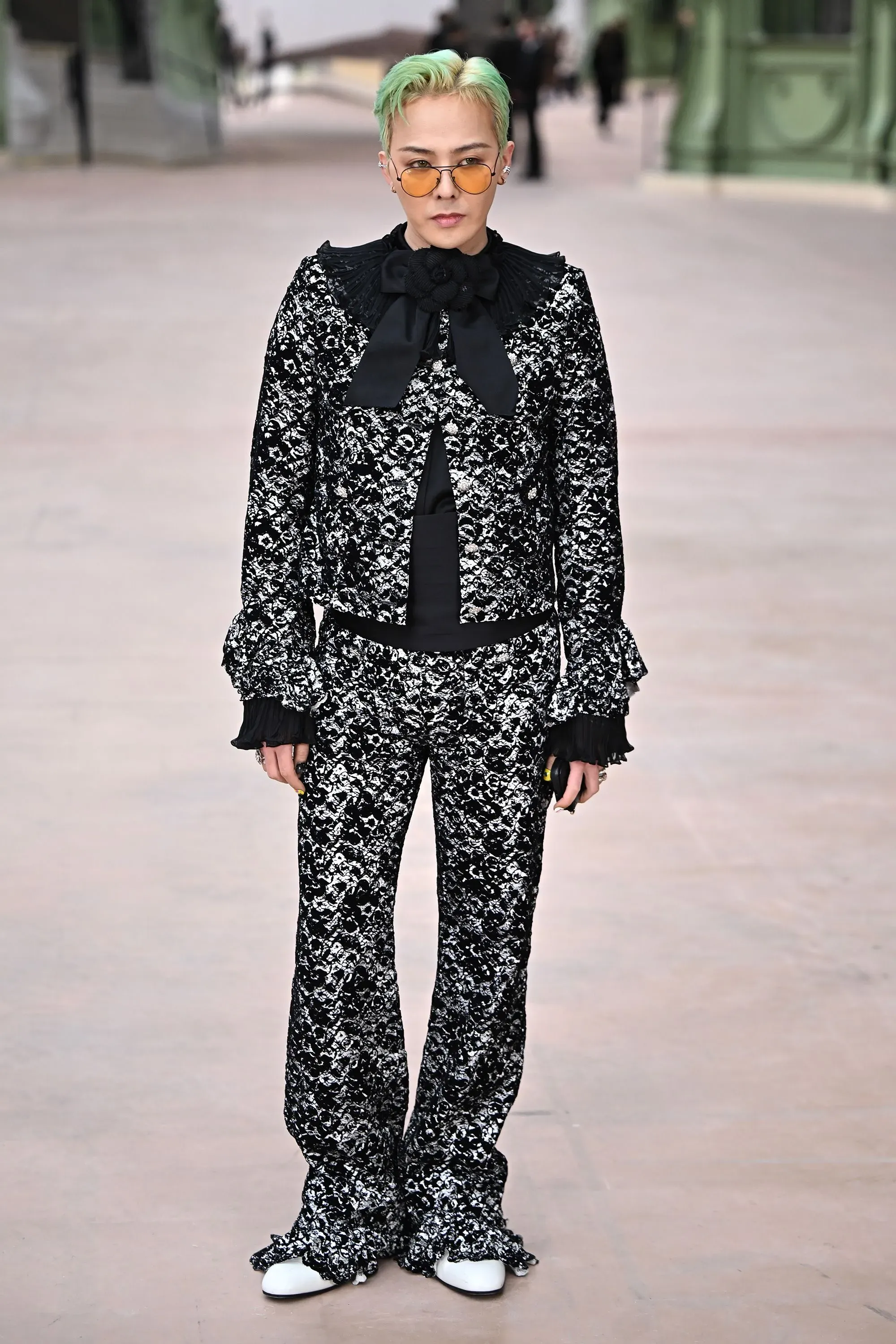 شخص يرتدي ملابس أنيقة ذات تصميم معقد، مع تسريحة شعر ملونة، في عرض أزياء يعكس تنوع أساليب الجمال في الثقافة الكورية.