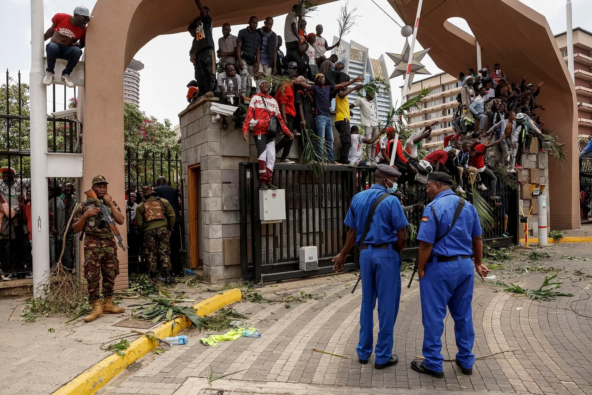 مشيعون يتجمعون حول بوابة أثناء جنازة رئيس الوزراء السابق رايلا أودينجا في نيروبي، مع وجود شرطة في الخلفية وأجواء من التوتر.