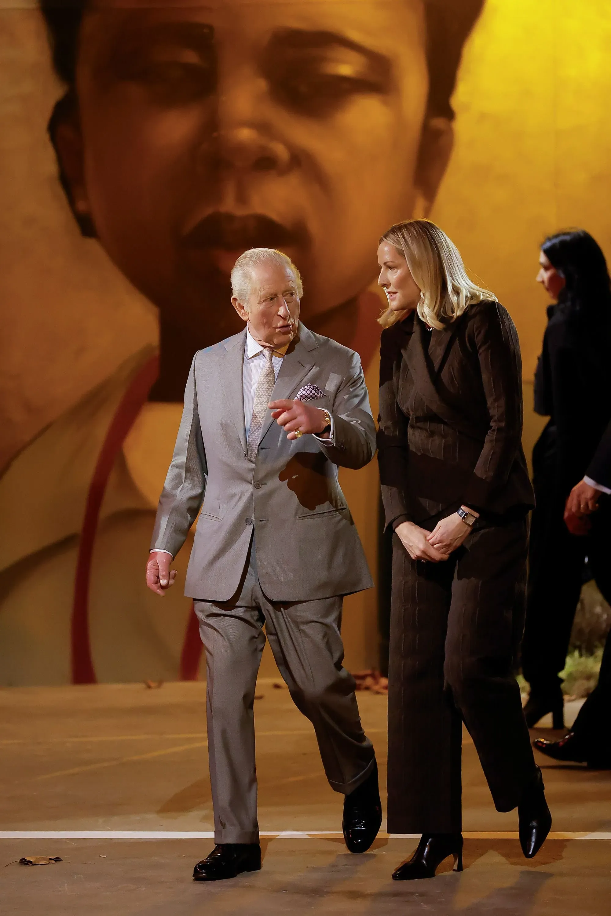 الملك تشارلز يتحدث مع سيدة في عرض أزياء تولو كوكر، مع خلفية فنية تعكس ثقافة الشتات الأفريقي.