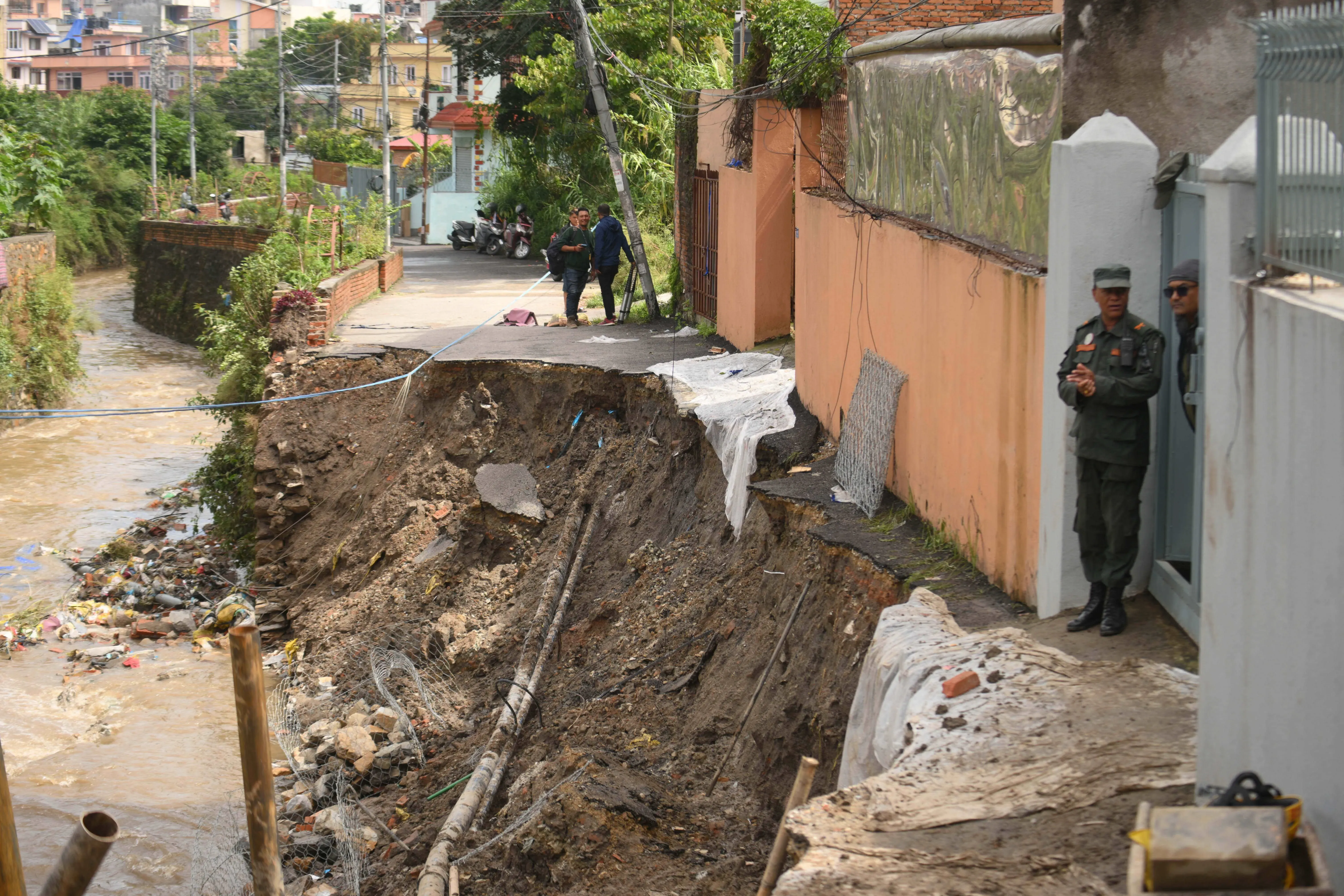 انهيار أرضي في نيبال تسبب في تدمير جزء من الطريق، مع وجود رجال أمن يقفون بالقرب من المنطقة المتضررة وسط الأضرار الناتجة عن الفيضانات.