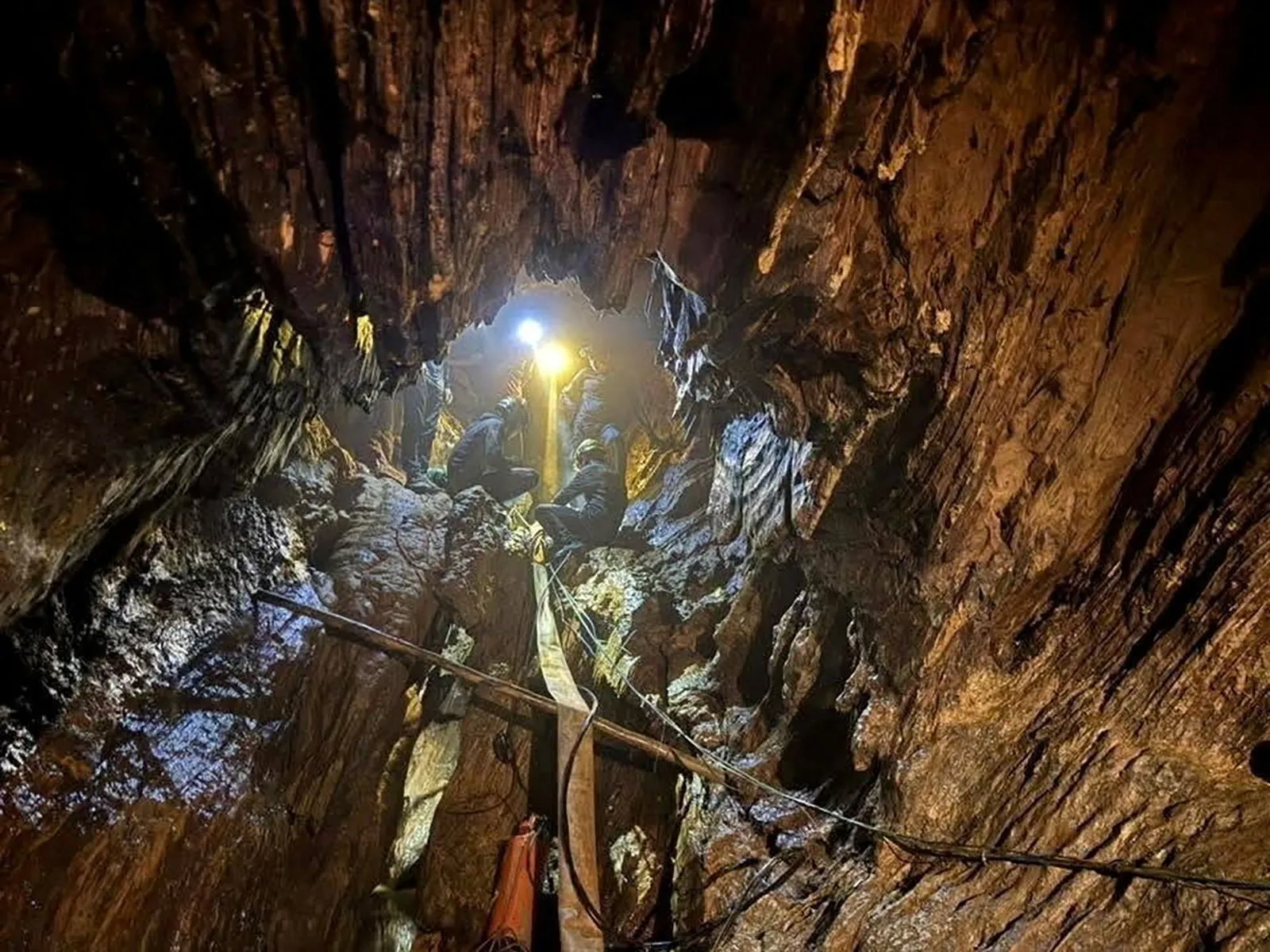صورة تظهر مجموعة من الرجال داخل كهف مظلم، حيث يضيء أحدهم بمصباح، محاطون بصخور رطبة، في سياق عملية إنقاذ بعد غمر المياه.