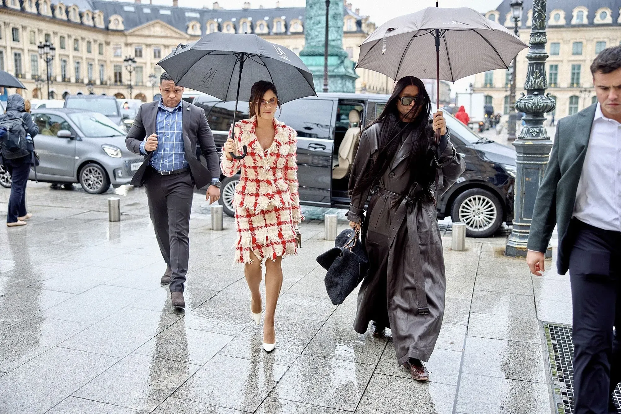 زوجان يحملان مظلات في شوارع باريس، حيث ترتدي المرأة فستانًا مزخرفًا بينما يرتدي الرجل بدلة رسمية، مع أجواء من الفخامة والأناقة.