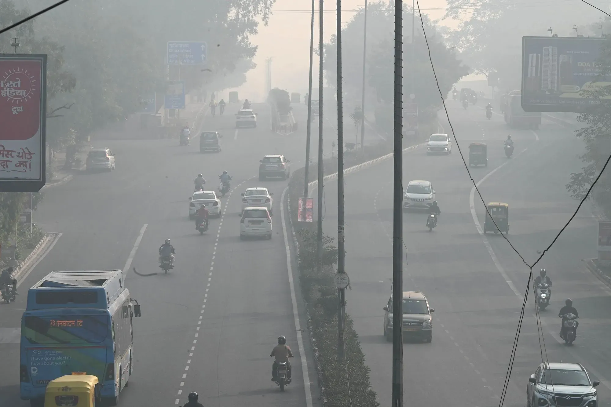 تظهر الصورة شارعًا في نيودلهي مغطى بسموم الضباب الدخاني، مع وجود سيارات ودراجات نارية تسير في ظروف رؤية منخفضة.