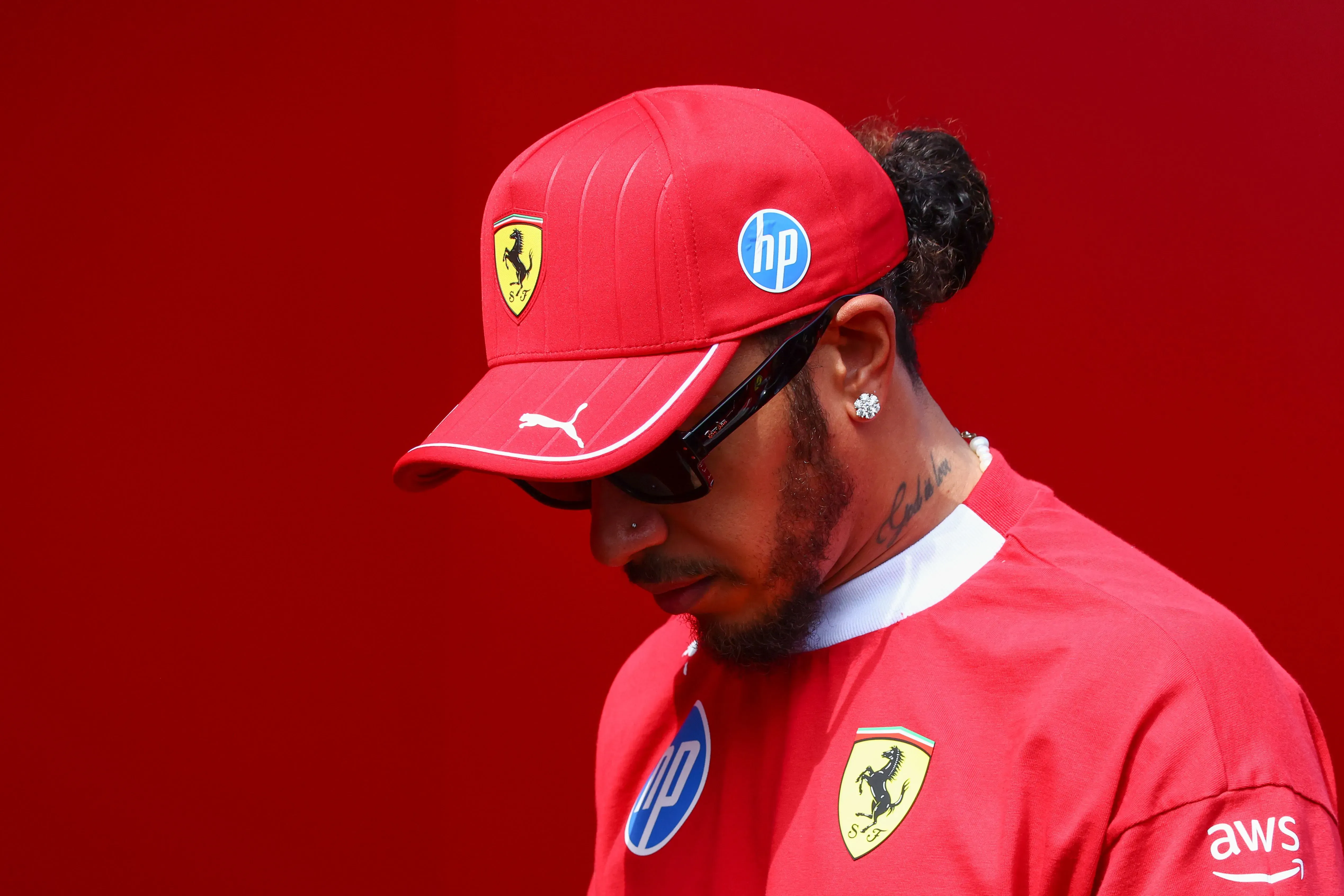 لويس هاميلتون يرتدي ملابس فريق فيراري، يبدو متأملاً وحزيناً، مع خلفية حمراء، بعد أداء مخيب في سباق الجائزة الكبرى المجري.