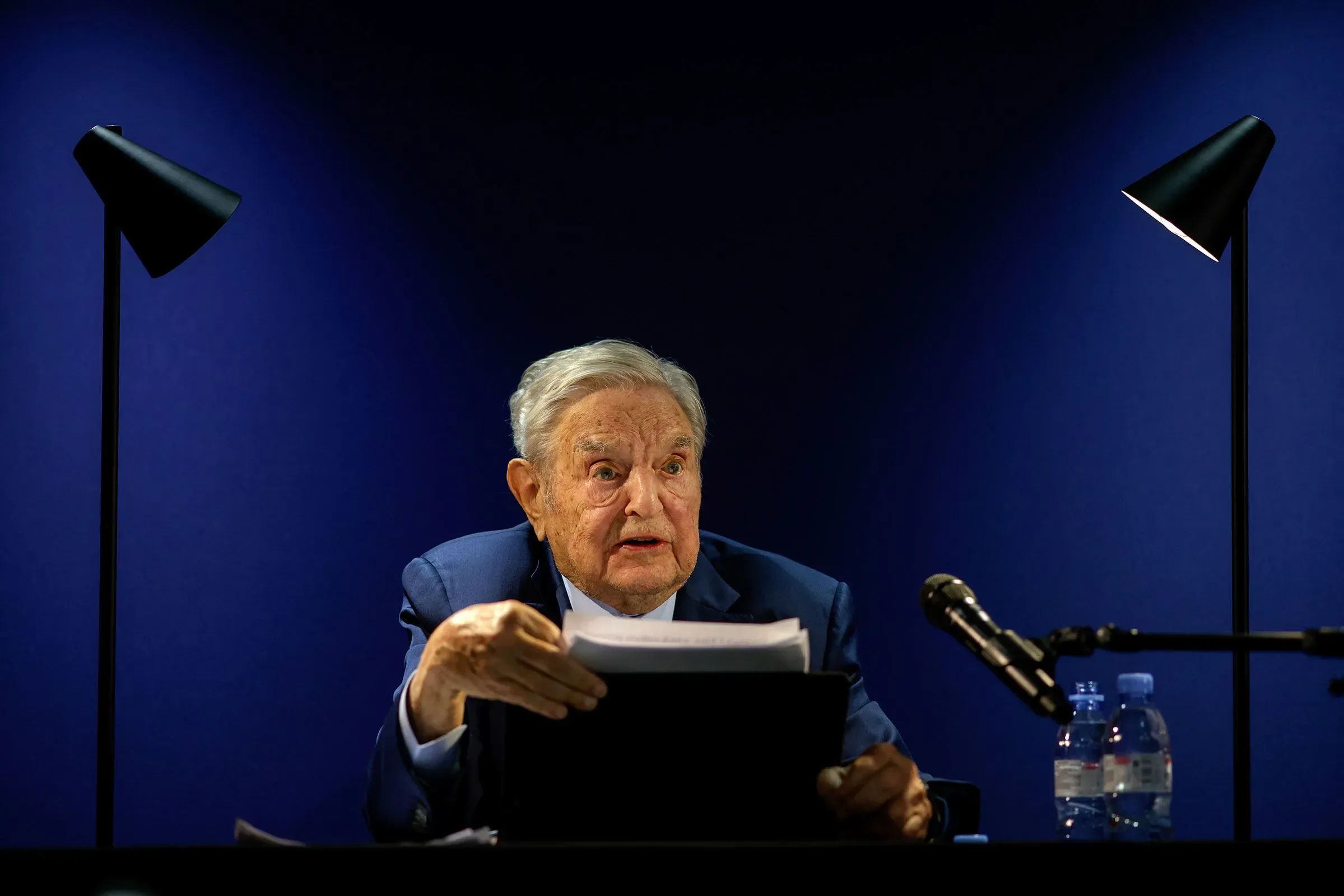 سوروس يتحدث في مؤتمر حول الأمن الديمقراطي، مع إضاءة خافتة، مع التركيز على القضايا التي تواجه المنظمات غير الربحية.