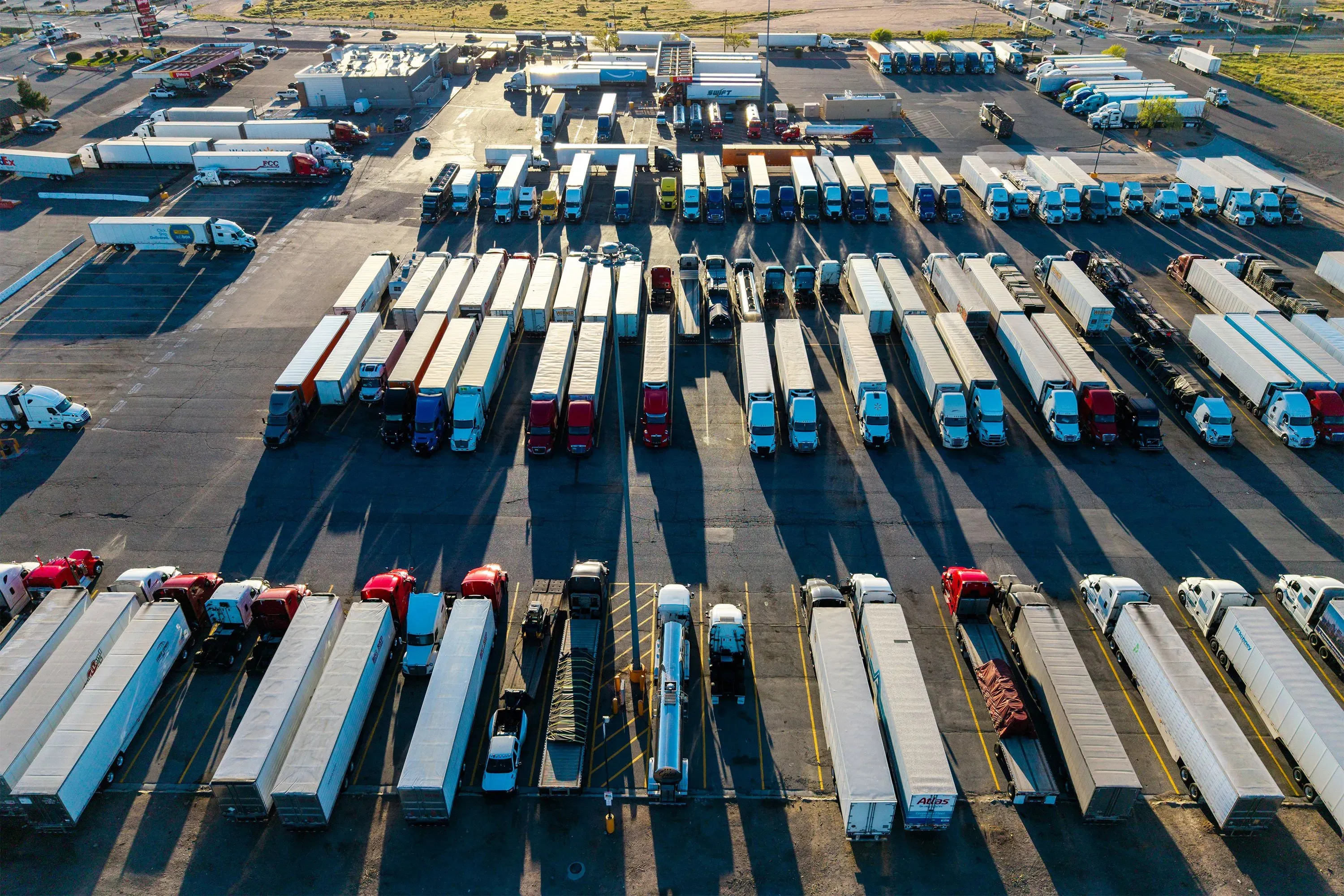 صف من الشاحنات الكبيرة المتوقفة في ساحة شحن، مع تباين الظلال على الأرض. تعكس الصورة أهمية النقل في نظام الطاقة العالمي.