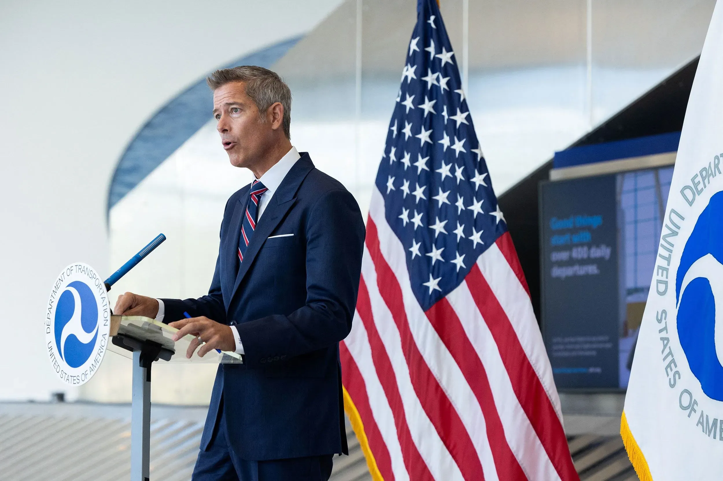 وزير النقل شون دافي يتحدث في مؤتمر صحفي بمطار فيلادلفيا، مع العلم الأمريكي وشعار وزارة النقل خلفه، حول تأثير الإغلاق الحكومي على تأخيرات الرحلات الجوية.