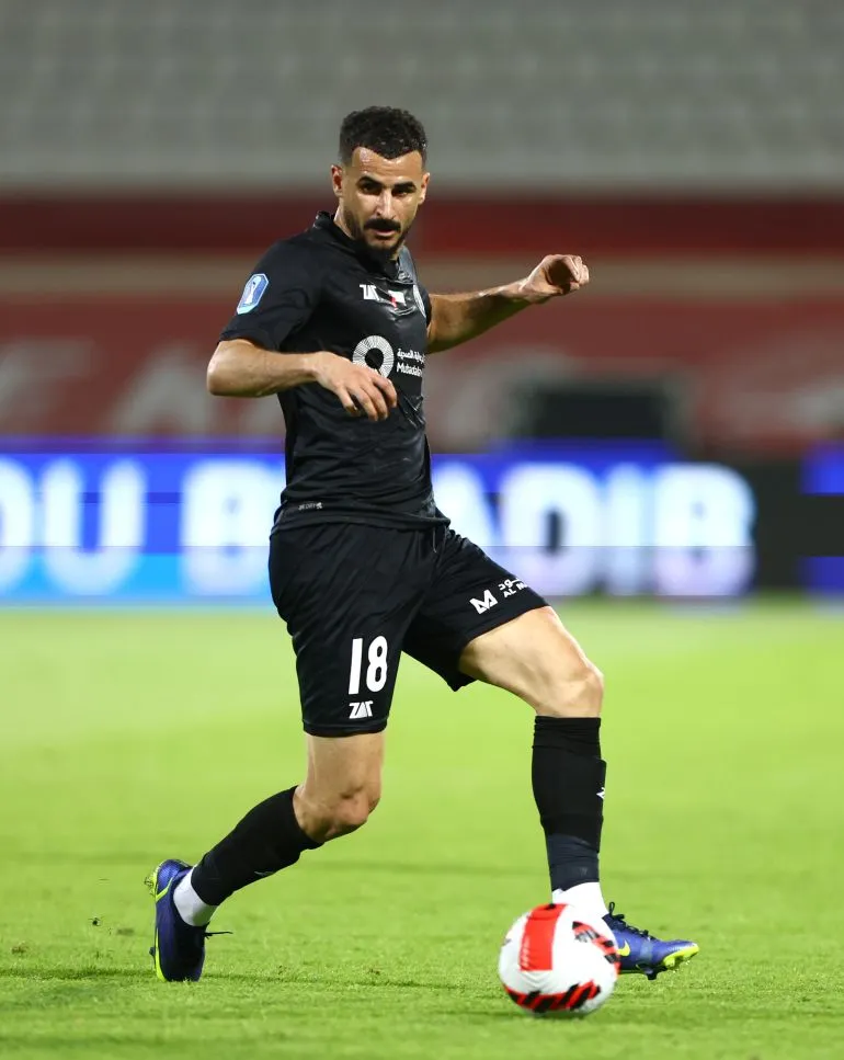 أيمن حسين، مهاجم منتخب العراق، أثناء اللعب في مباراة، يرتدي زي الفريق الأسود ويحمل الكرة، مع أجواء تنافسية في الخلفية.