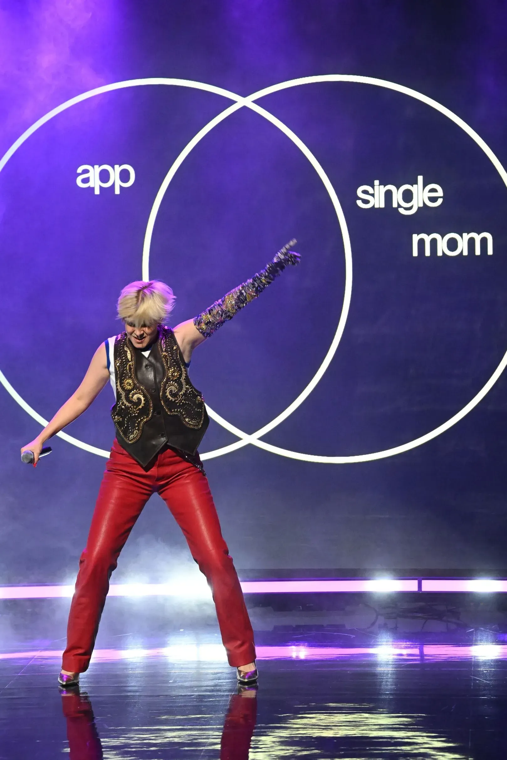 روبن تؤدي أغنيتها "Sexistential" مرتدية سروالًا جلديًا أحمر وقميصًا أبيض مع صدرية جلدية مزخرفة، في عرض ديناميكي على المسرح.