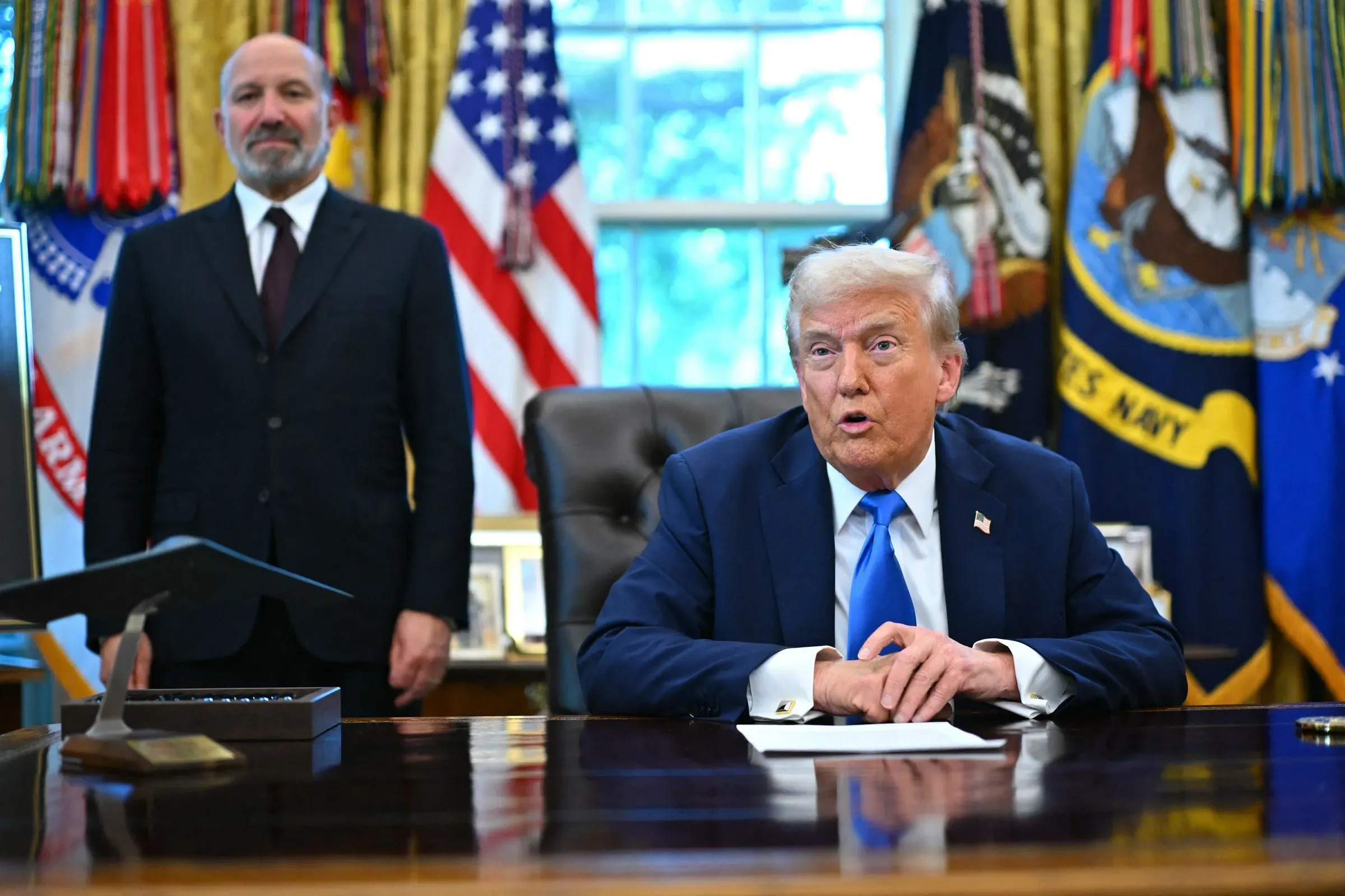 صورة لوزير التجارة الأمريكي هوارد لوتنيك يتحدث في المكتب البيضاوي، مع وجود شخص آخر خلفه. تعكس الصورة الأجواء الرسمية للحدث.