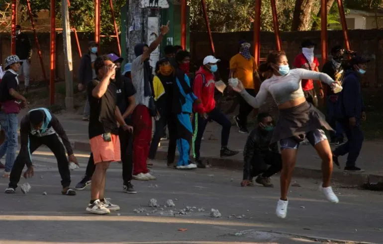 محتجون يرتدون أقنعة في شوارع مدغشقر، يشاركون في مظاهرة ضد الحكومة، مع وجود امرأة تقفز وتحمل حجرًا، تعبيرًا عن الغضب.