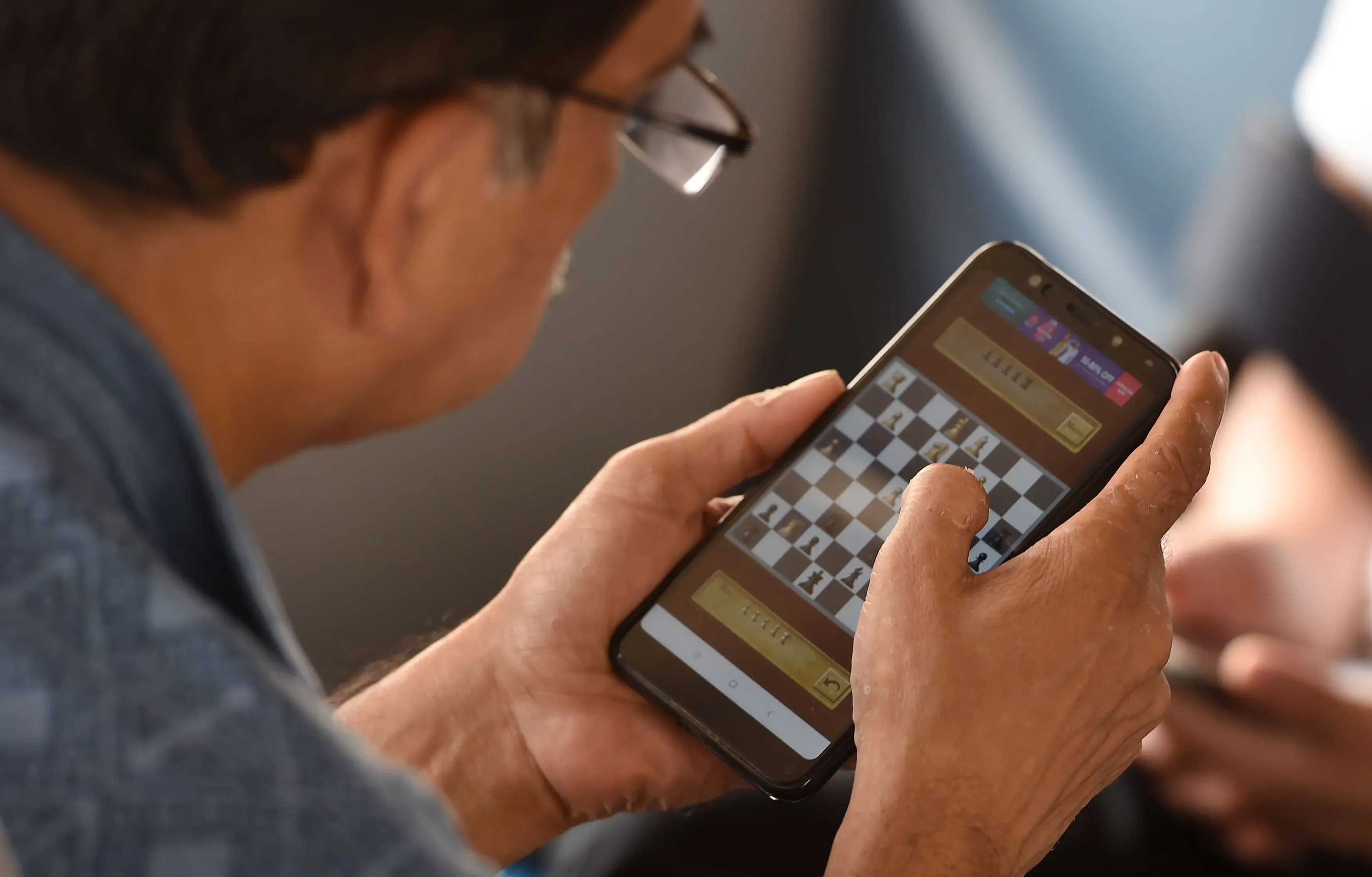 رجل يلعب الشطرنج عبر تطبيق على هاتفه المحمول، مع التركيز على اللوحة الرقمية، مما يعكس التحول الرقمي للعبة.