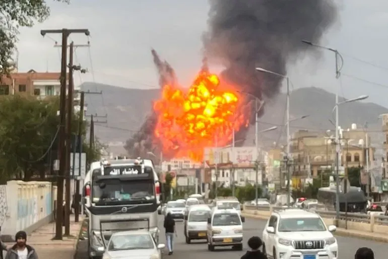 انفجار قوي يتصاعد منه الدخان والنيران في منطقة حضرية، مع وجود سيارات في الشارع وأشخاص يراقبون الحادث.