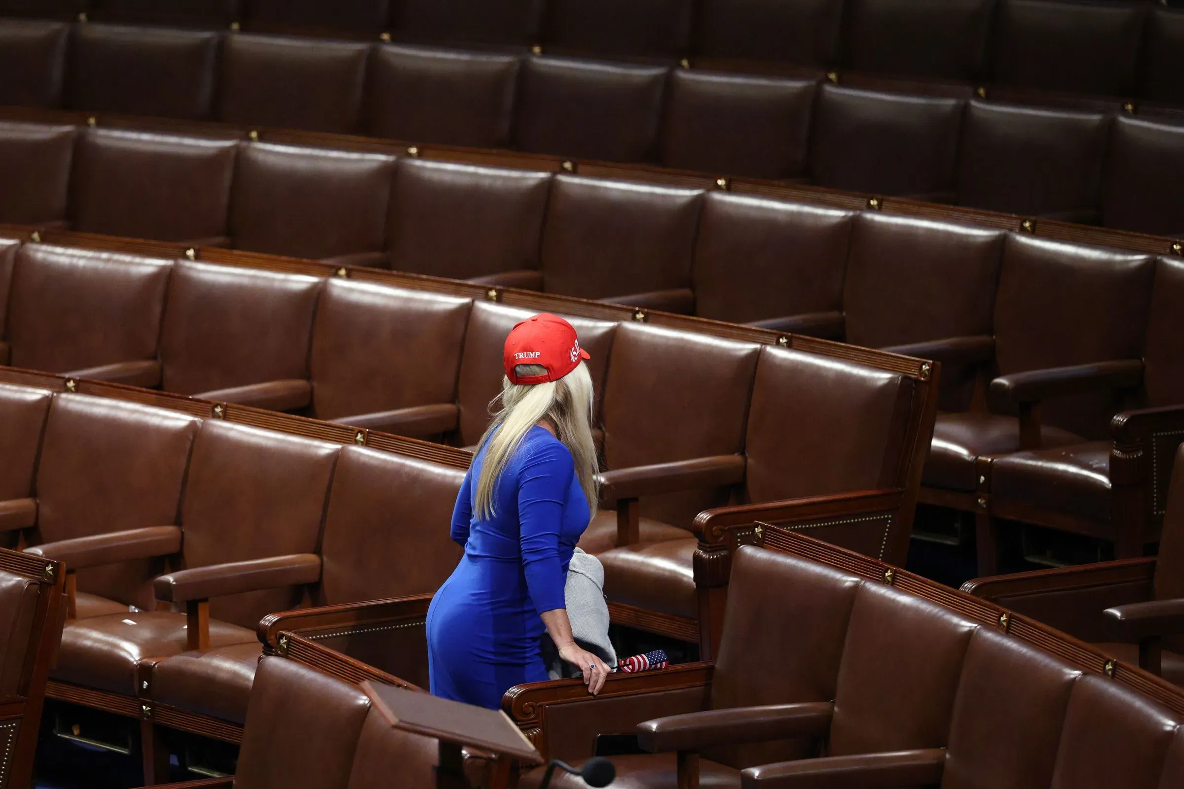 امرأة ترتدي قبعة تحمل شعار ترامب، تتواجد في قاعة فارغة بمجلس النواب، تعكس حالة التوتر السياسي داخل الحزب الجمهوري.