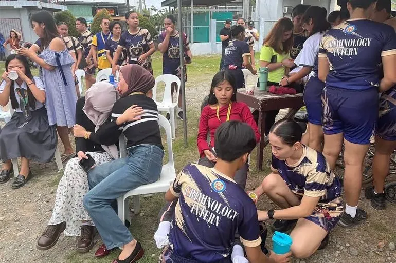 طلاب يتجمعون في منطقة آمنة بعد الزلزال في الفلبين، يظهرون مشاعر القلق والدعم المتبادل وسط جهود الإغاثة.