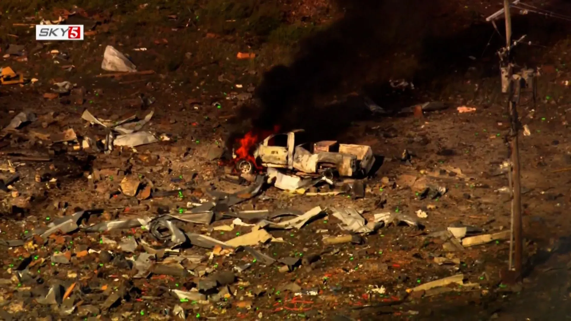 حطام منشأة عسكرية في تينيسي بعد انفجار مدمر، مع سيارة مشتعلة وسط debris، مما يعكس خطورة الحادث وتأثيره على المنطقة.