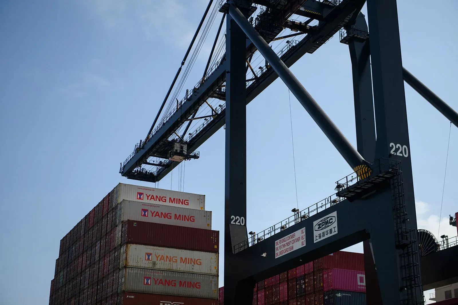 صورة لميناء شحن يحتوي على حاويات ملونة، تُظهر رافعة عملاقة ترفع حاوية من بين حاويات أخرى، تعكس التحديات في التجارة الدولية.