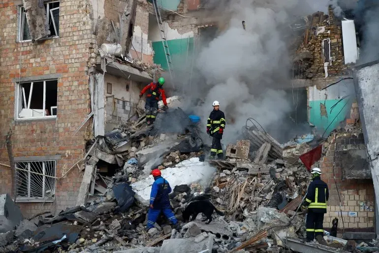 فرق الإنقاذ تعمل في موقع هجوم روسي على مبنى سكني في كييف، حيث تظهر الأنقاض والدخان بعد الانفجارات.