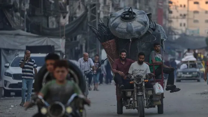 شبان يحملون أمتعة ثقيلة على دراجة نارية في شوارع غزة المزدحمة، وسط أجواء من الفوضى بعد الهجمات الإسرائيلية.