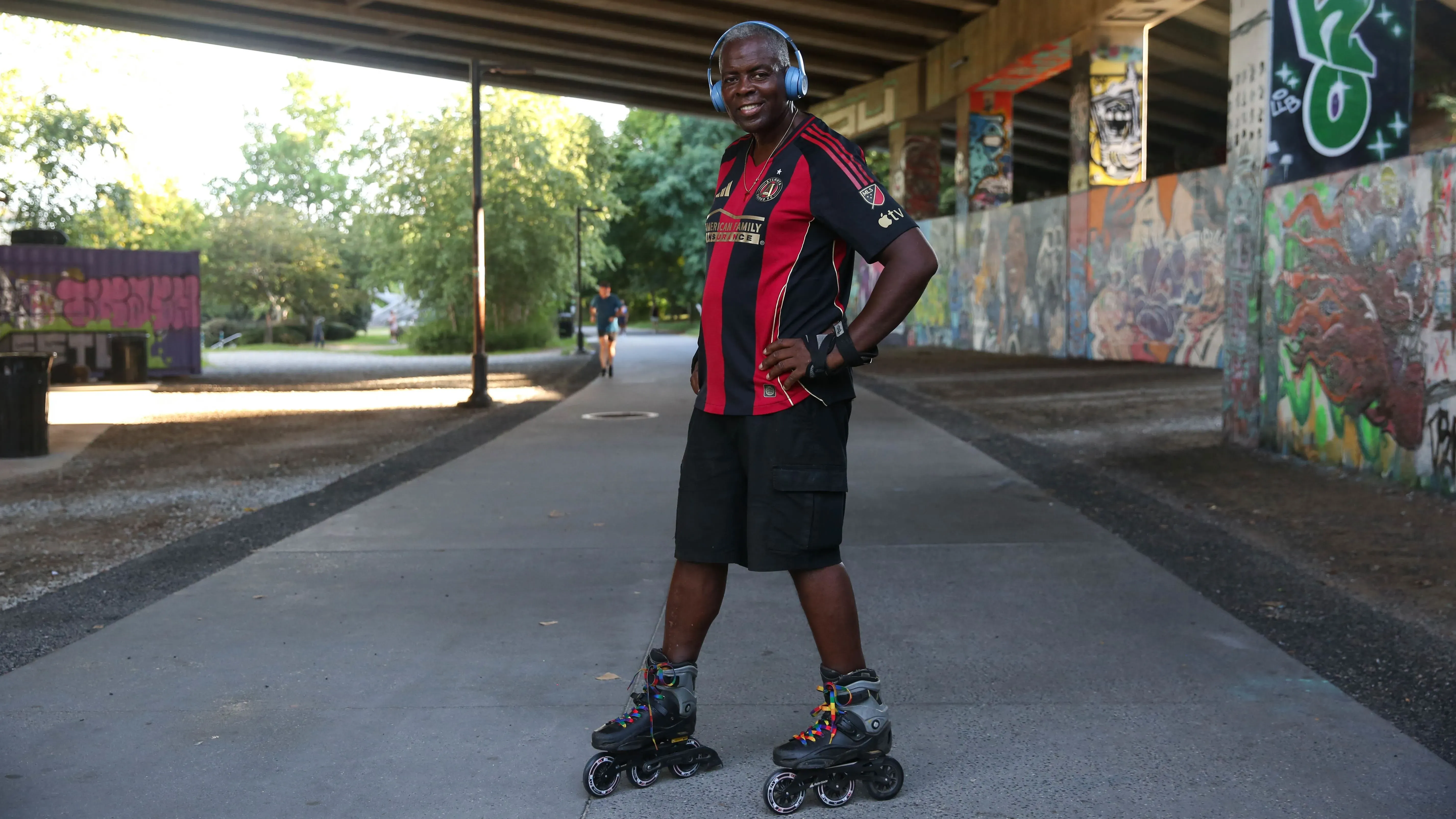 كيفن راندولف، البالغ من العمر 61 عاماً، يتزلج على العجلات في بيلت لاين بأتلانتا، مرتدياً سماعات رأس وقميص رياضي، وسط جدران مزينة بالرسوم الجدارية.