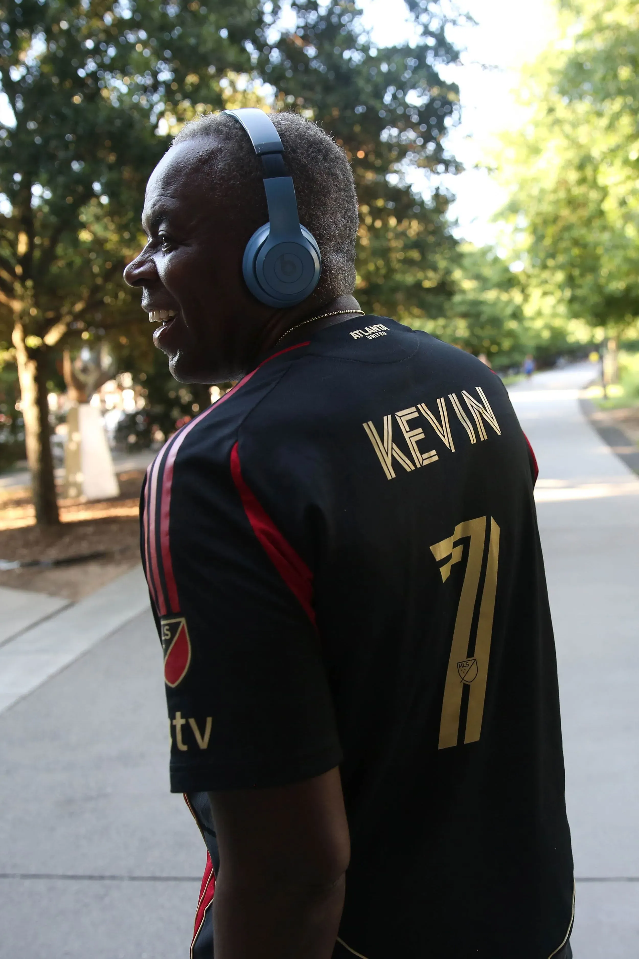 كيفن راندولف، رجل مسن يرتدي سماعات رأس، مبتسم أثناء تجوله على بيلت لاين في أتلانتا، حيث يشارك في الغناء والتفاعل مع المارة.