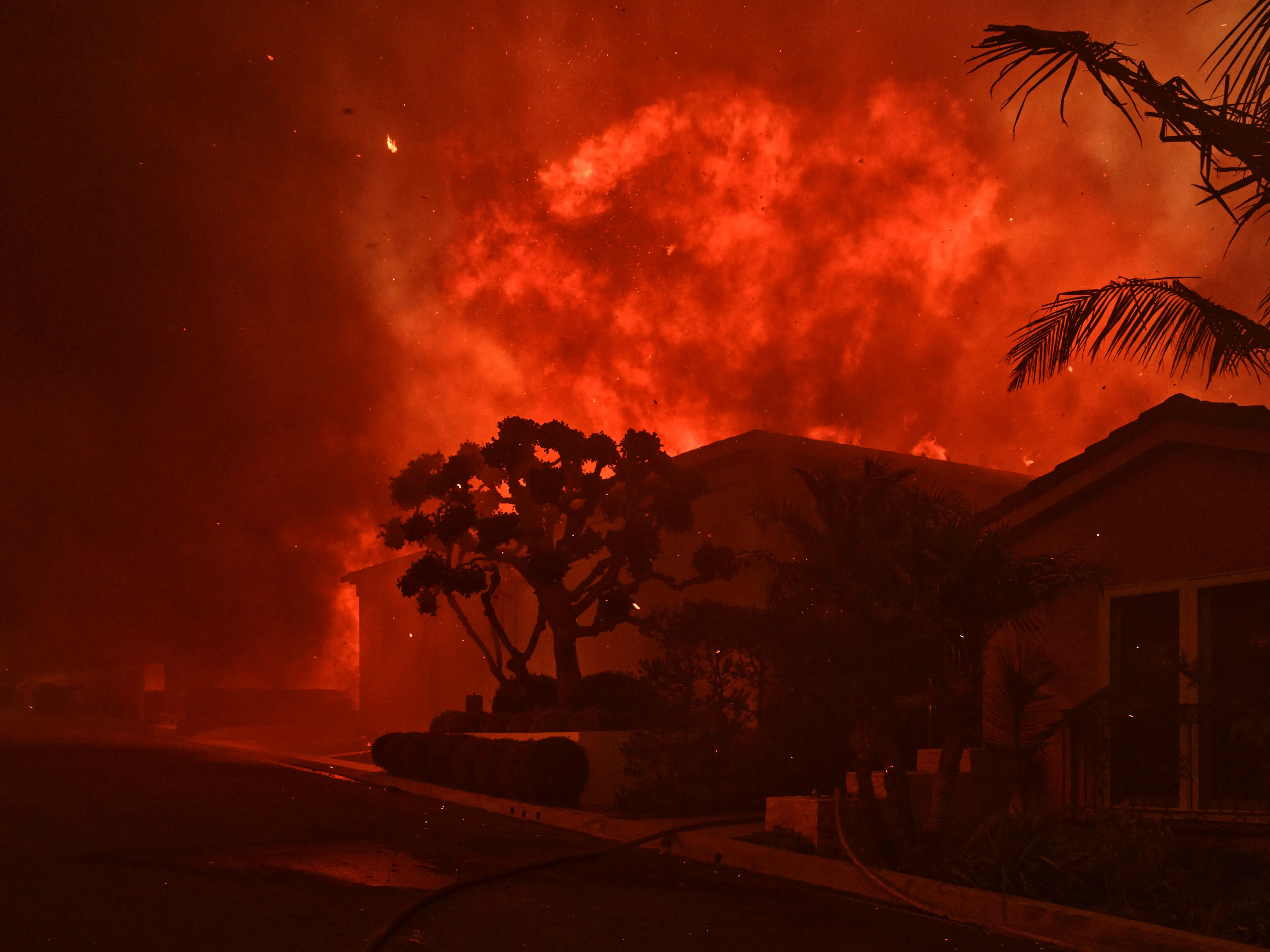 مشهد لحرائق الغابات في كاليفورنيا، حيث تتصاعد النيران والدخان فوق المنازل، مما يبرز خطر حرائق الغابات المتزايد في المنطقة.