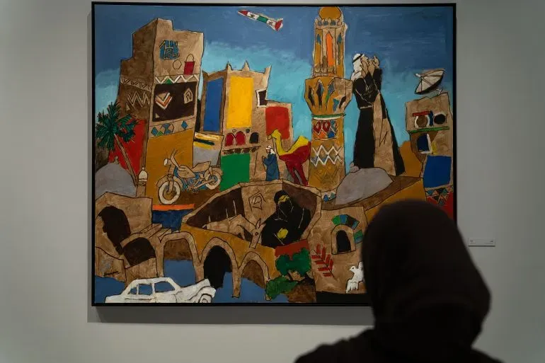 لوحة ملونة للفنان مقبول فدا حسين تُظهر مشهدًا حضريًا نابضًا بالحياة، مع تفاصيل معمارية وعناصر ثقافية تعكس إرثه الفني.