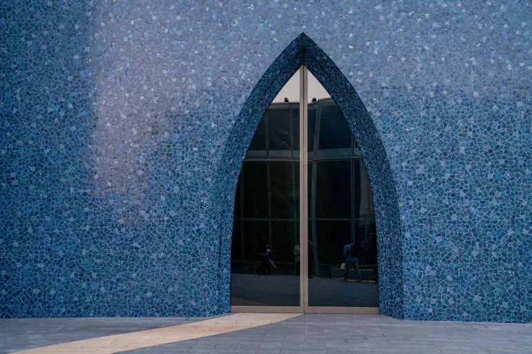 واجهة متحف "لوح وقلم" في الدوحة، بتصميم عصري وجدران زرقاء، تعكس التراث الفني لمقبول فدا حسين وأعماله المعاصرة.