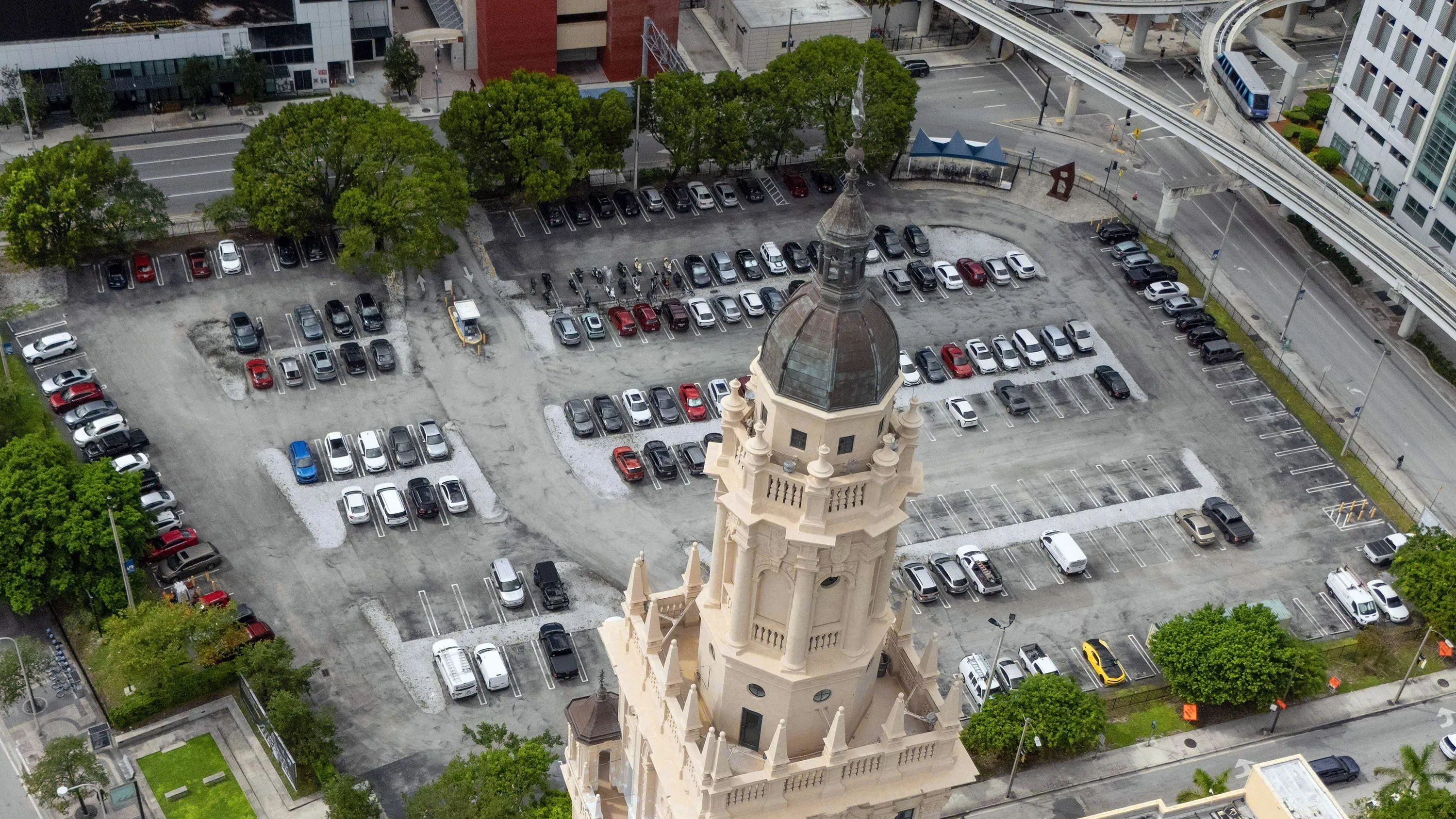 صورة جوية لموقف سيارات واسع في ميامي، يظهر فيه العديد من السيارات، مع برج تاريخي في الزاوية، يرمز إلى تاريخ المدينة.
