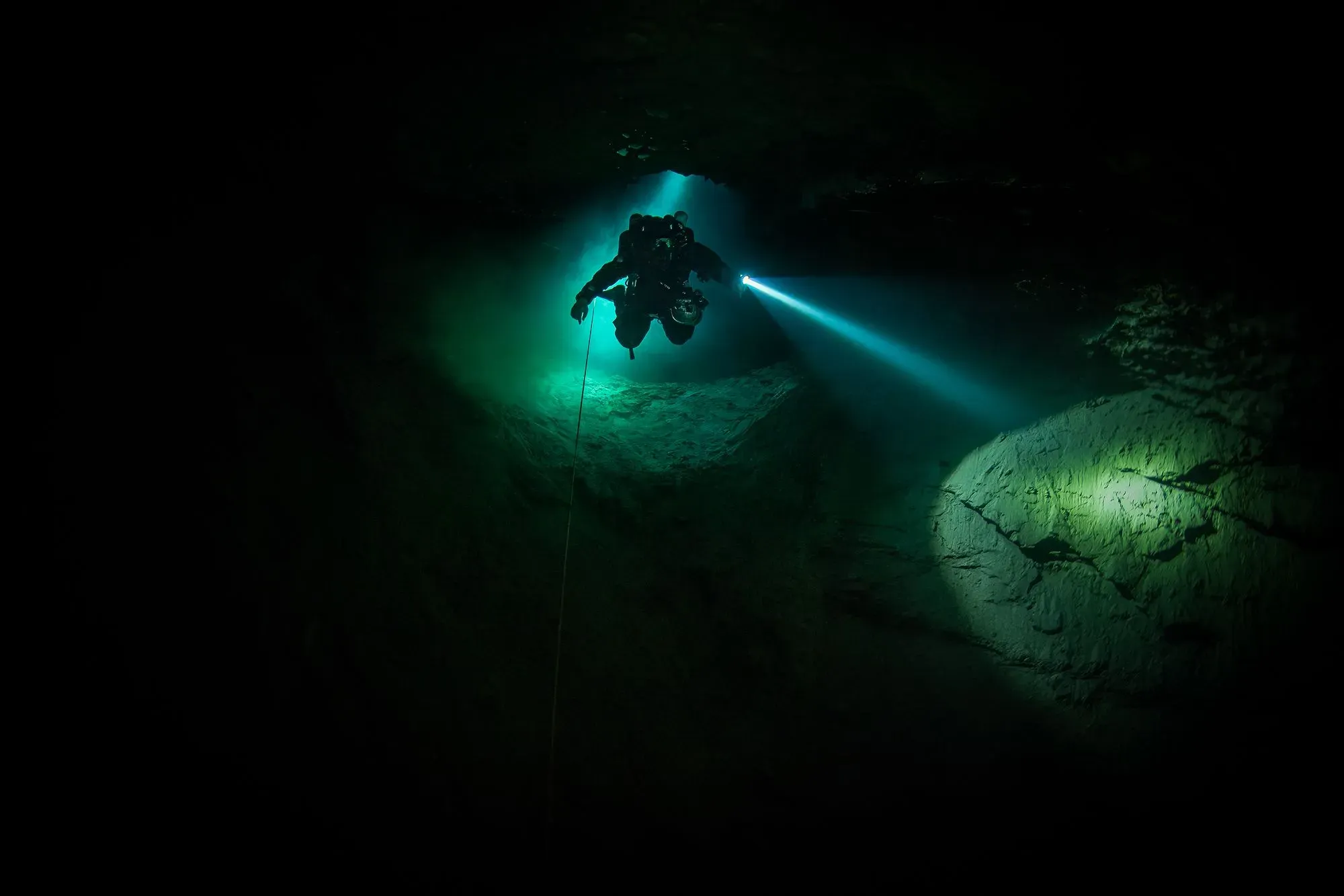 غواص يستكشف كهف مولنار يانوس في بودابست، حيث تتلألأ الأضواء في المياه الدافئة والظلام الدامس، مما يكشف عن جمال البيئة تحت الأرض.