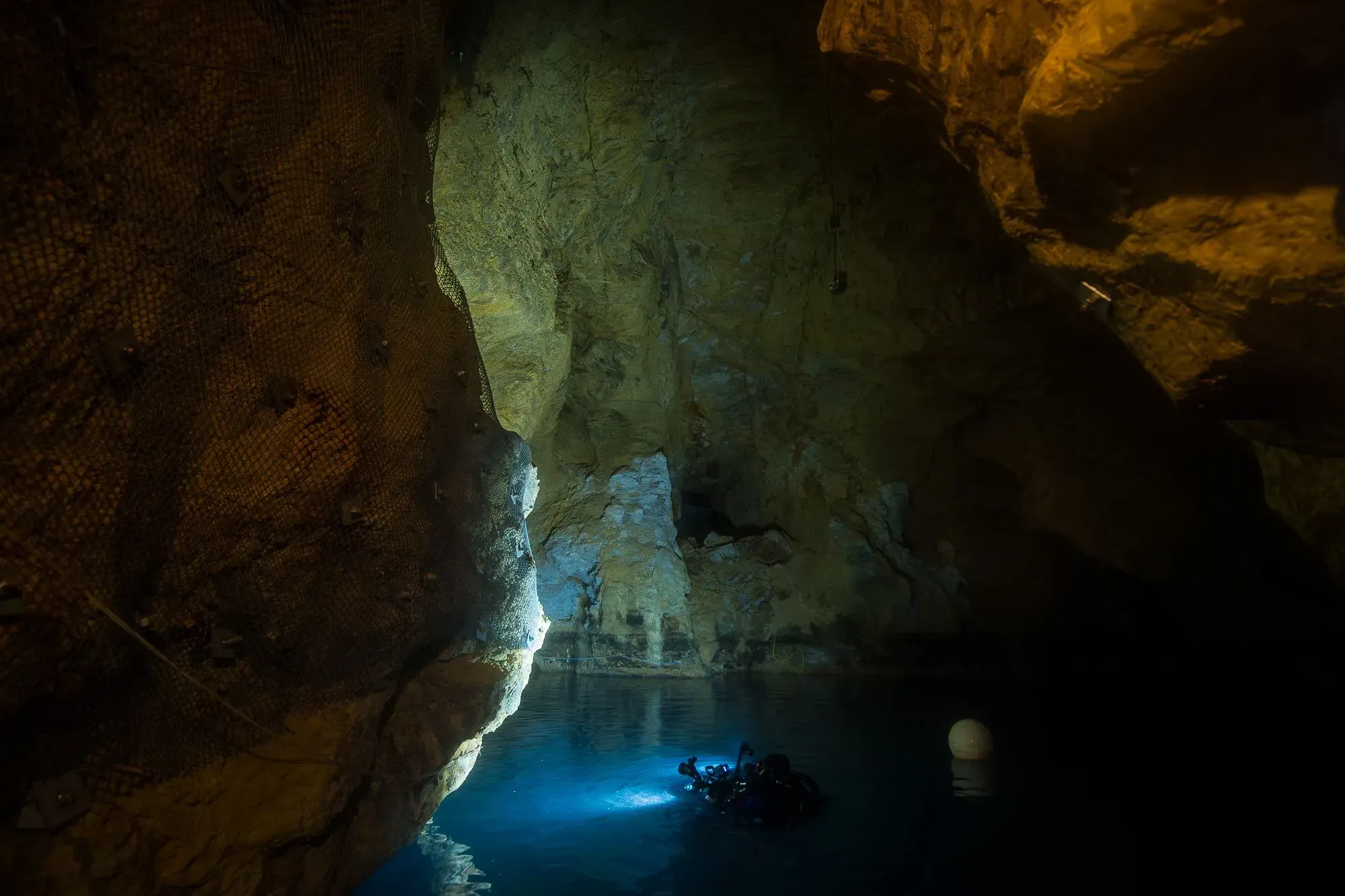 مدخل كهف مولنار يانوس تحت الماء في بودابست، حيث ينغمر الغواصون في مياه دافئة بينما تتلألأ الأضواء في الظلام.