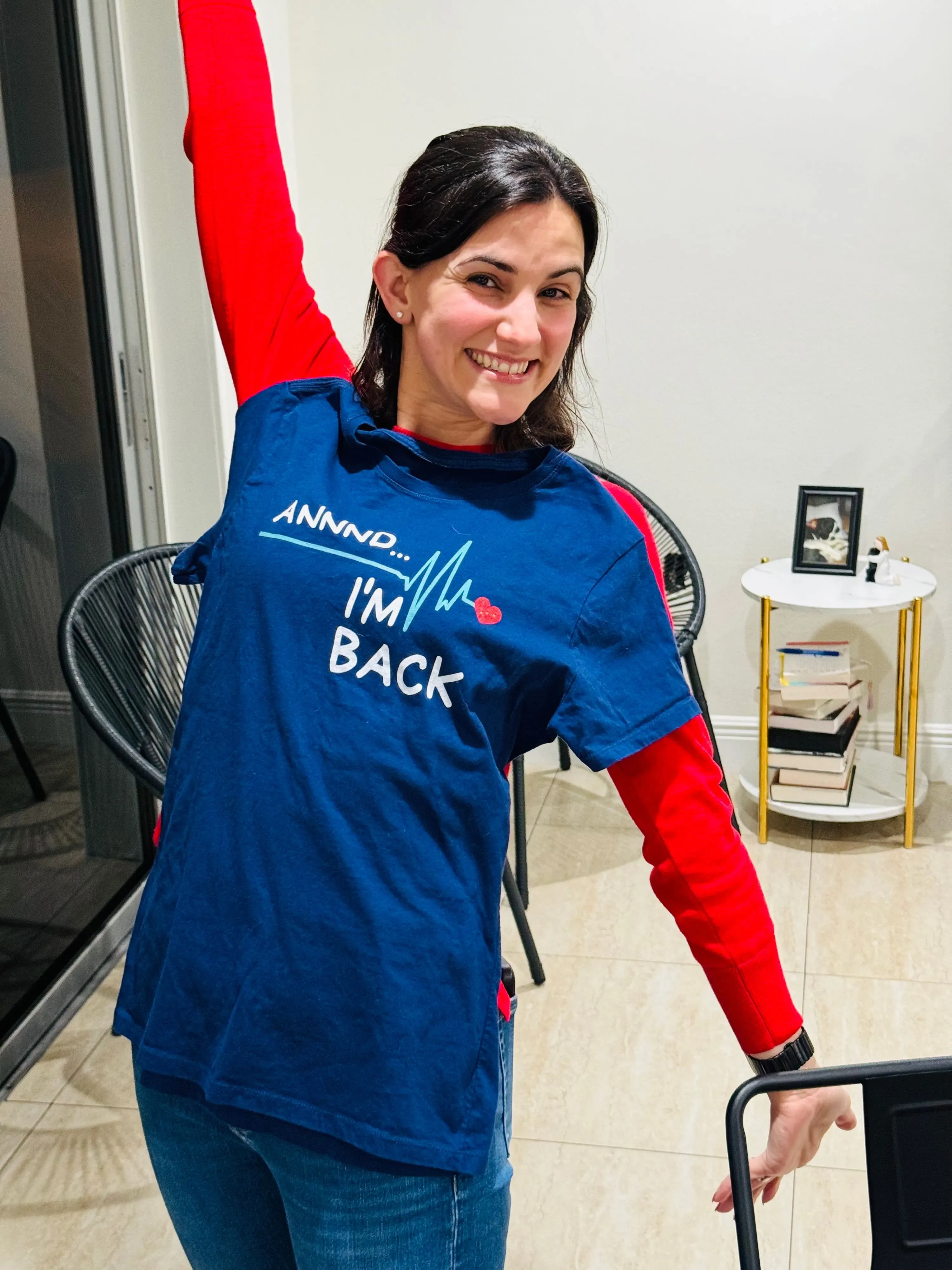 امرأة مبتسمة ترتدي قميصًا أزرق مكتوبًا عليه "I'm BACK"، ترفع ذراعها في إشارة إيجابية. تعكس الصورة روح التفاؤل والصحة في سياق توجيهات جديدة حول علاج الكوليسترول.