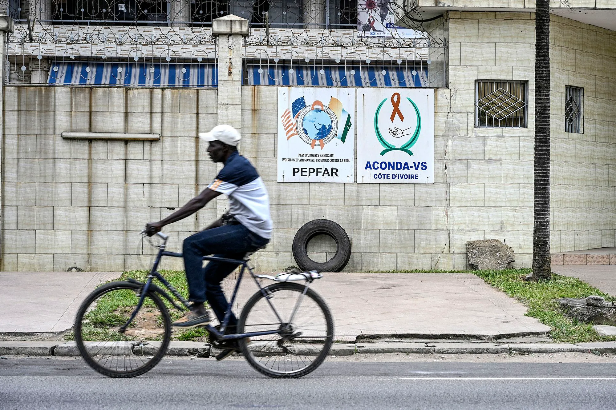 رجل يقود دراجة أمام لافتة لمبادرة PEPFAR الأمريكية لمكافحة الإيدز في ساحل العاج، في ظل مخاوف من توقف تمويل برامج مكافحة فيروس نقص المناعة.