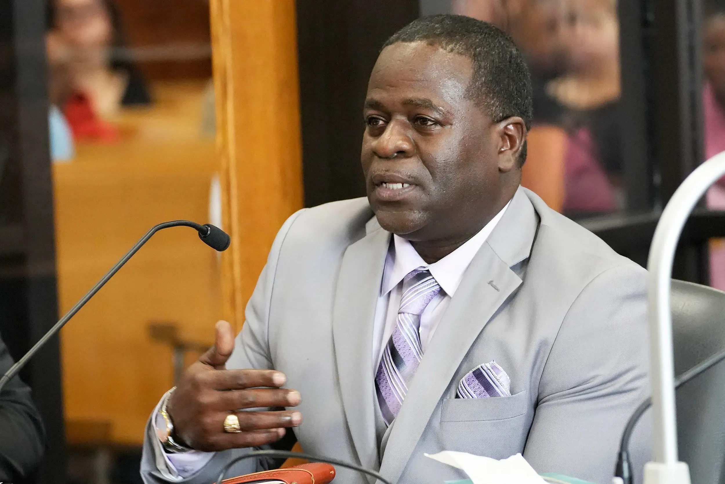 رجل يرتدي بدلة رمادية يتحدث في المحكمة، مع تعبيرات وجه تعكس الجدية أثناء جلسة النطق بالحكم في قضية قتل.