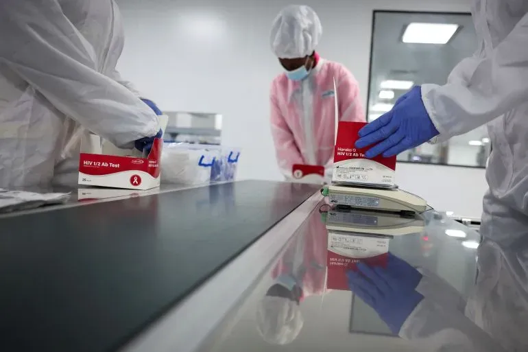 فنيون صحيون يرتدون ملابس واقية يقومون بتجهيز اختبارات فيروس نقص المناعة البشرية في مختبر، مما يعكس الجهود العالمية لمواجهة التحديات الصحية.