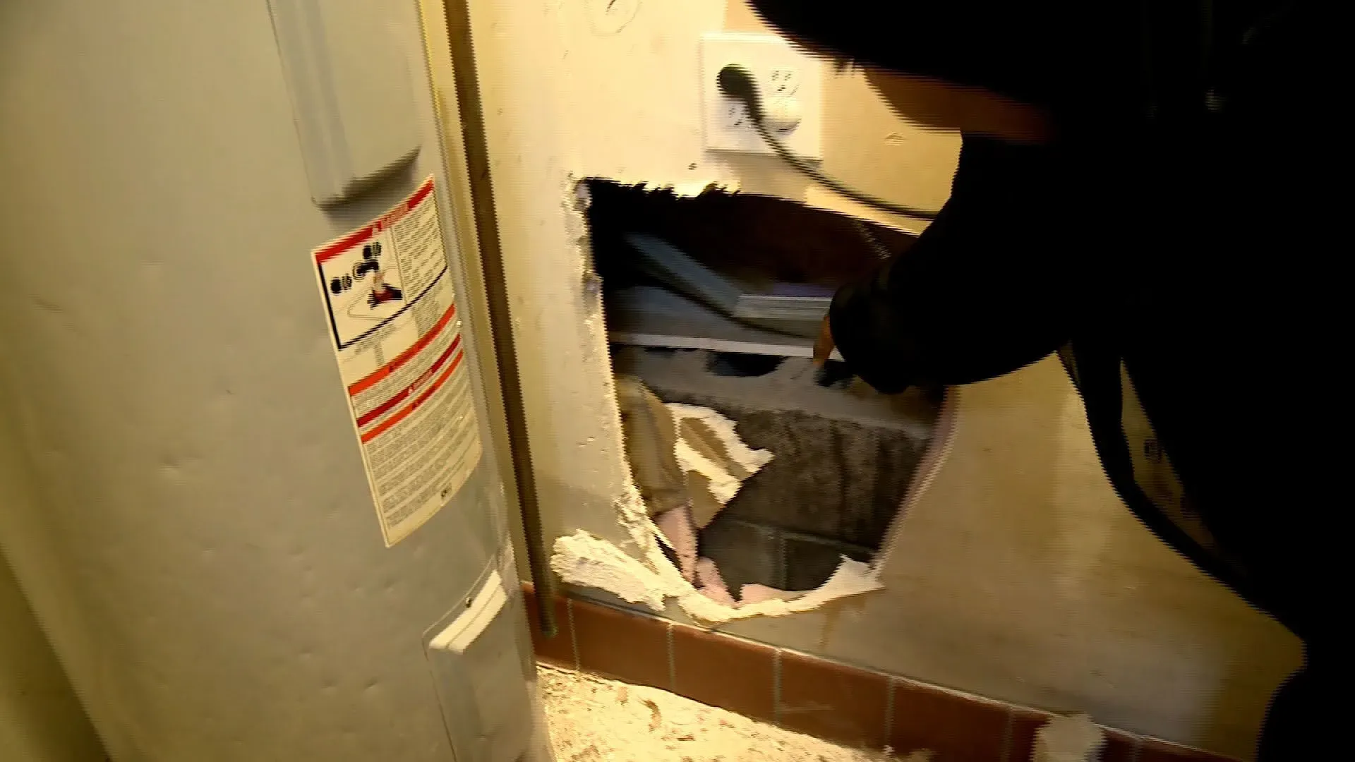 فتحة في جدار تظهر آثار تآكل، بينما يشير شخص إلى الداخل. تعكس الصورة القلق بشأن تحقيقات الاحتيال في مراكز رعاية الأطفال في مينيسوتا.