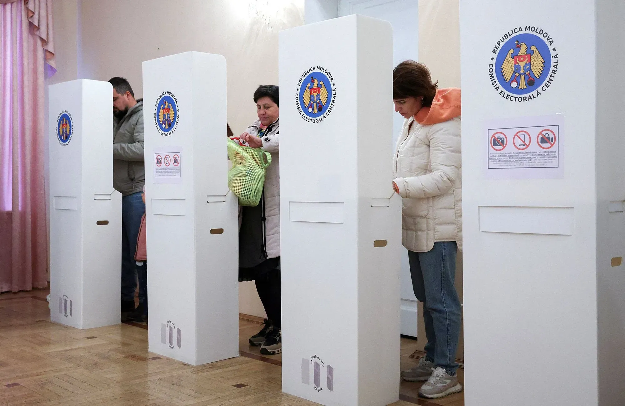 مواطنون مولدوفيون يصوتون في مركز انتخابي، مع وجود صناديق الاقتراع والشعارات الرسمية، في سياق الانتخابات البرلمانية التي تدعم الانضمام إلى الاتحاد الأوروبي.