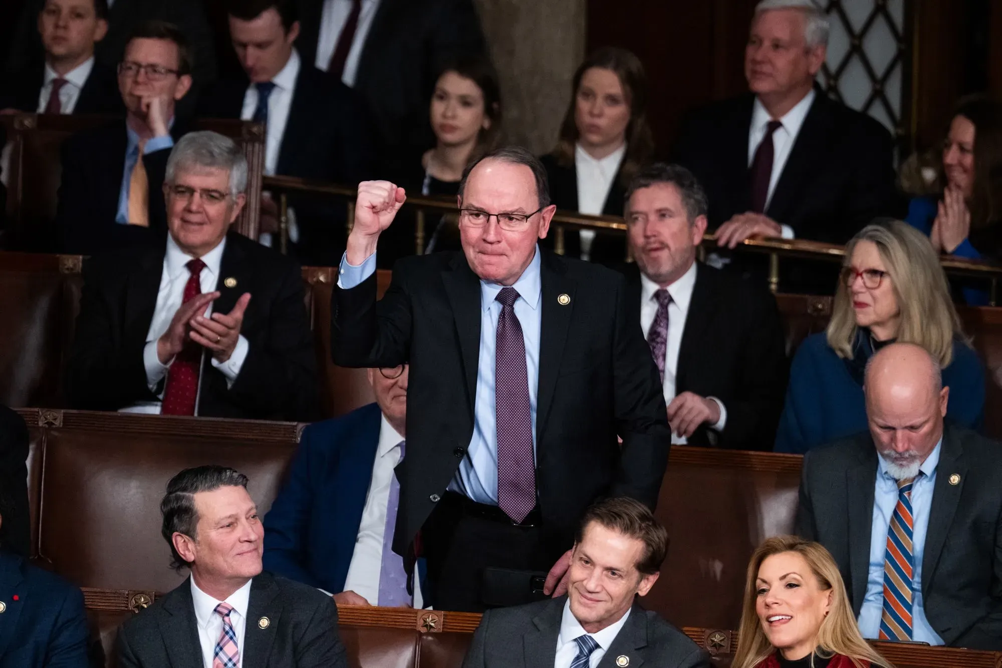 نائب جمهوري يرفع يده في قاعة الكونغرس وسط زملائه، مع تعبير عن الحماس خلال جلسة رسمية.