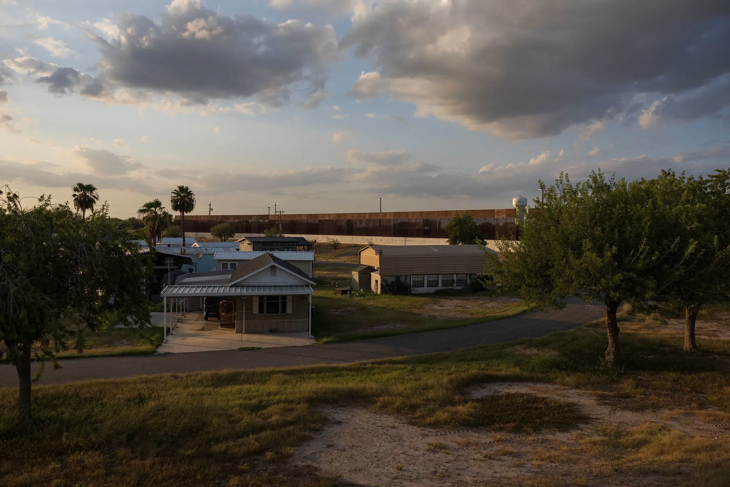 منظر لبلدة صغيرة في تكساس مع منازل وشجيرات، وخلفها جدار حدودي، يعكس التغيرات السياسية وتأثيرها على المجتمع المحلي.